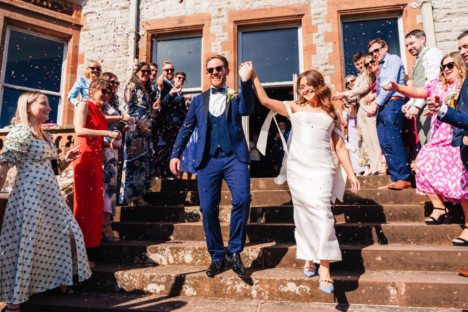 Castle Leslie Wedding Photographer Dublin Wedding party celebrating on stone steps outside historic building on sunny day.