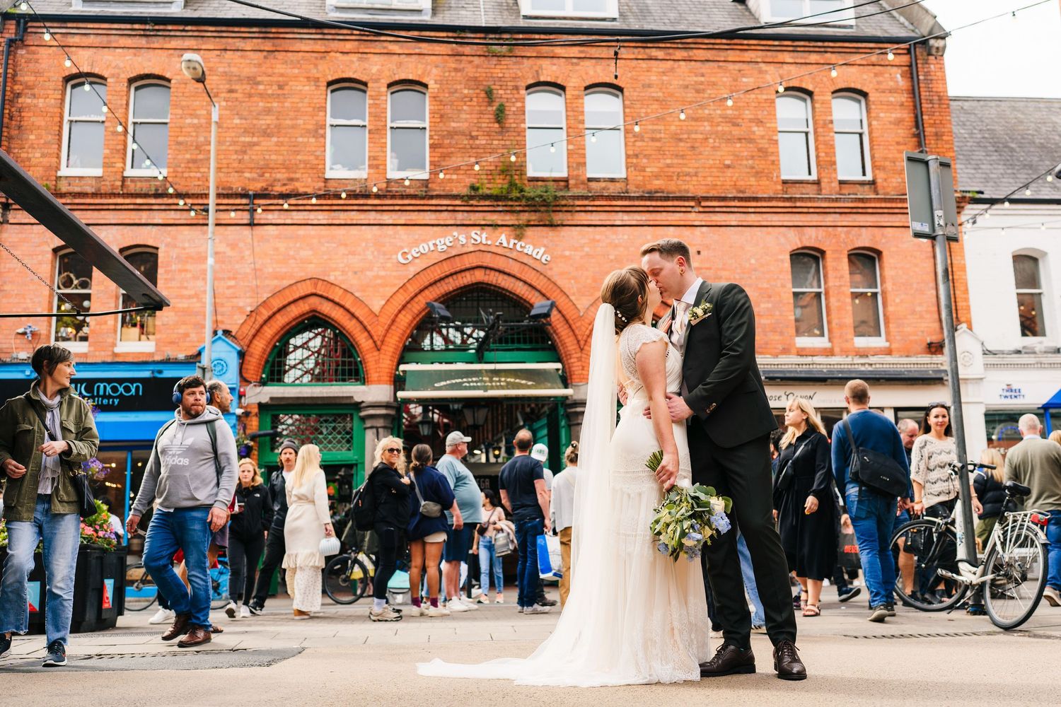 A wedding scene outside a historic red brick building with arched windows and a crowd of onlookers. PHOTOGRAPHER Dublin Ireland Wedding