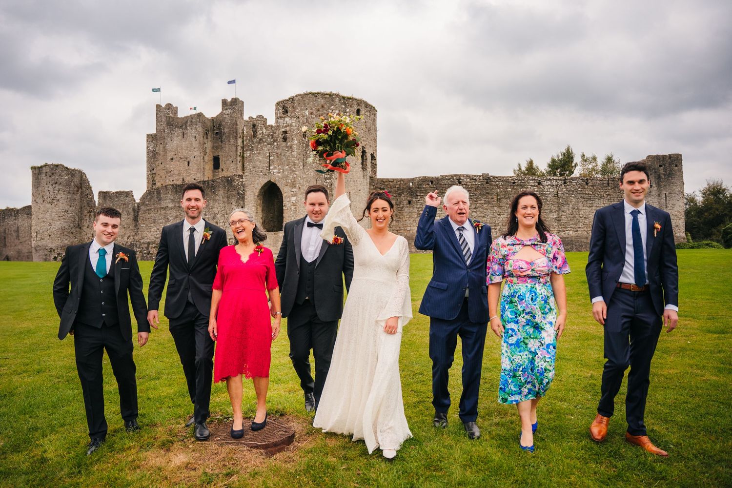 Wedding party poses on the lawn in front of a historic castle on a cloudy day. Wedding Photography Trim Castle Ireland