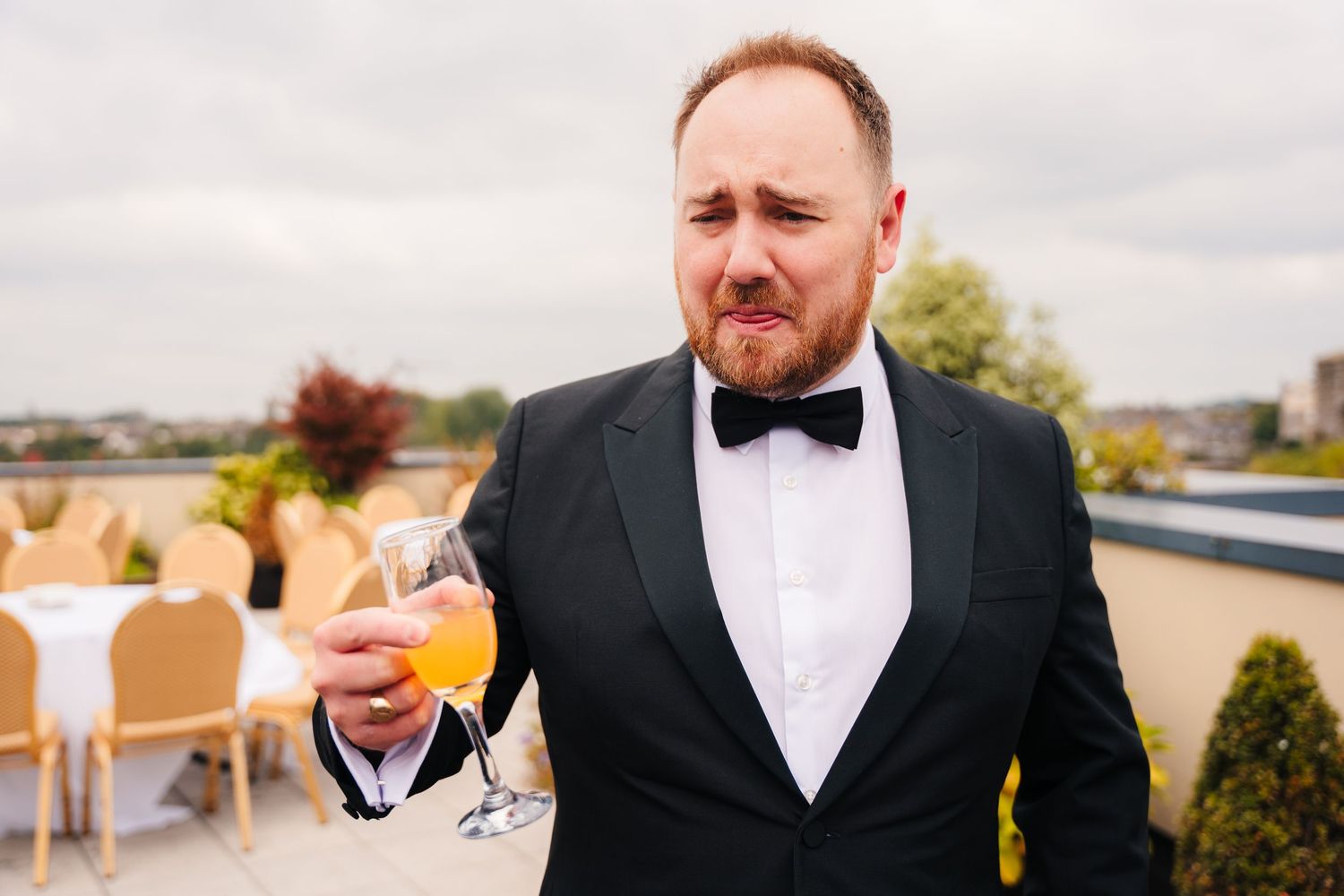 Gentleman in a black tuxedo and bowtie holds a glass of champagne on an outdoor terrace. Wedding Photography Trim Castle Ireland