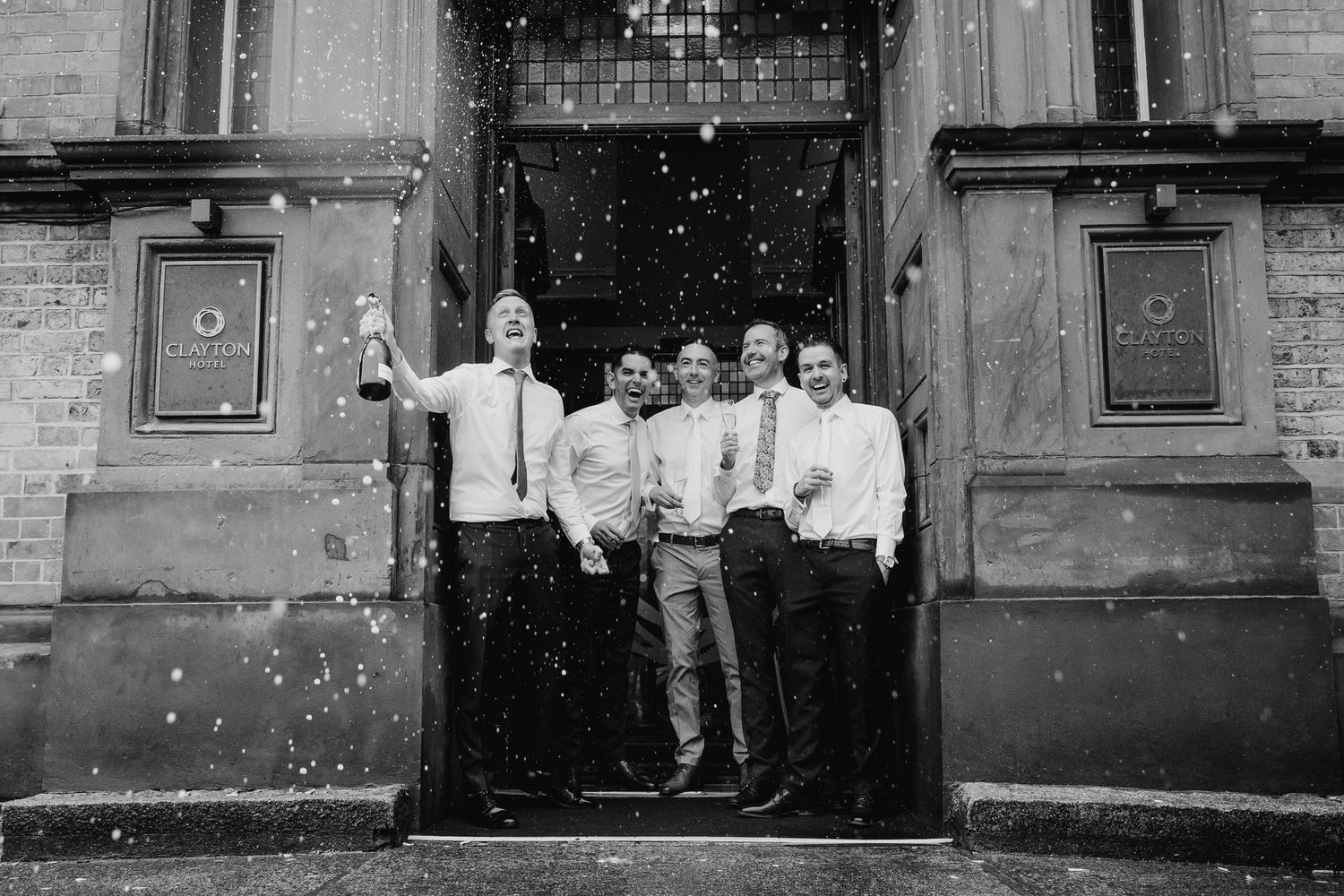 Black and white panoramic shot of wedding guests throwing confetti outside a historic stone building. Wedding photographer dublin
