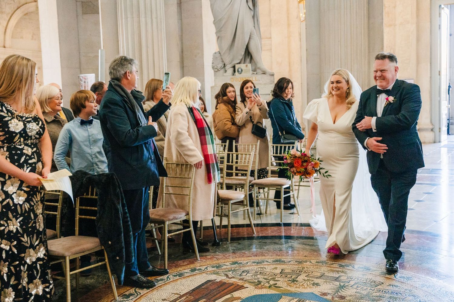 Elegant wedding reception guests seated at long tables in an ornate ballroom with marble columns and decorative details. Wedding photographe