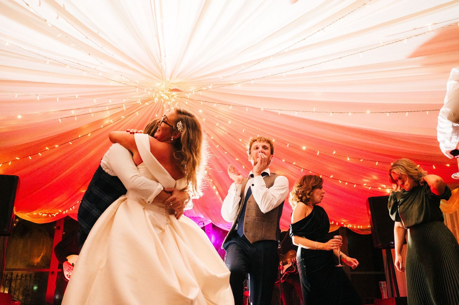 Couple dancing under a red-lit marquee tent at their wedding reception with guests in the background.  Virginia Park Lodge Wedding Photograp