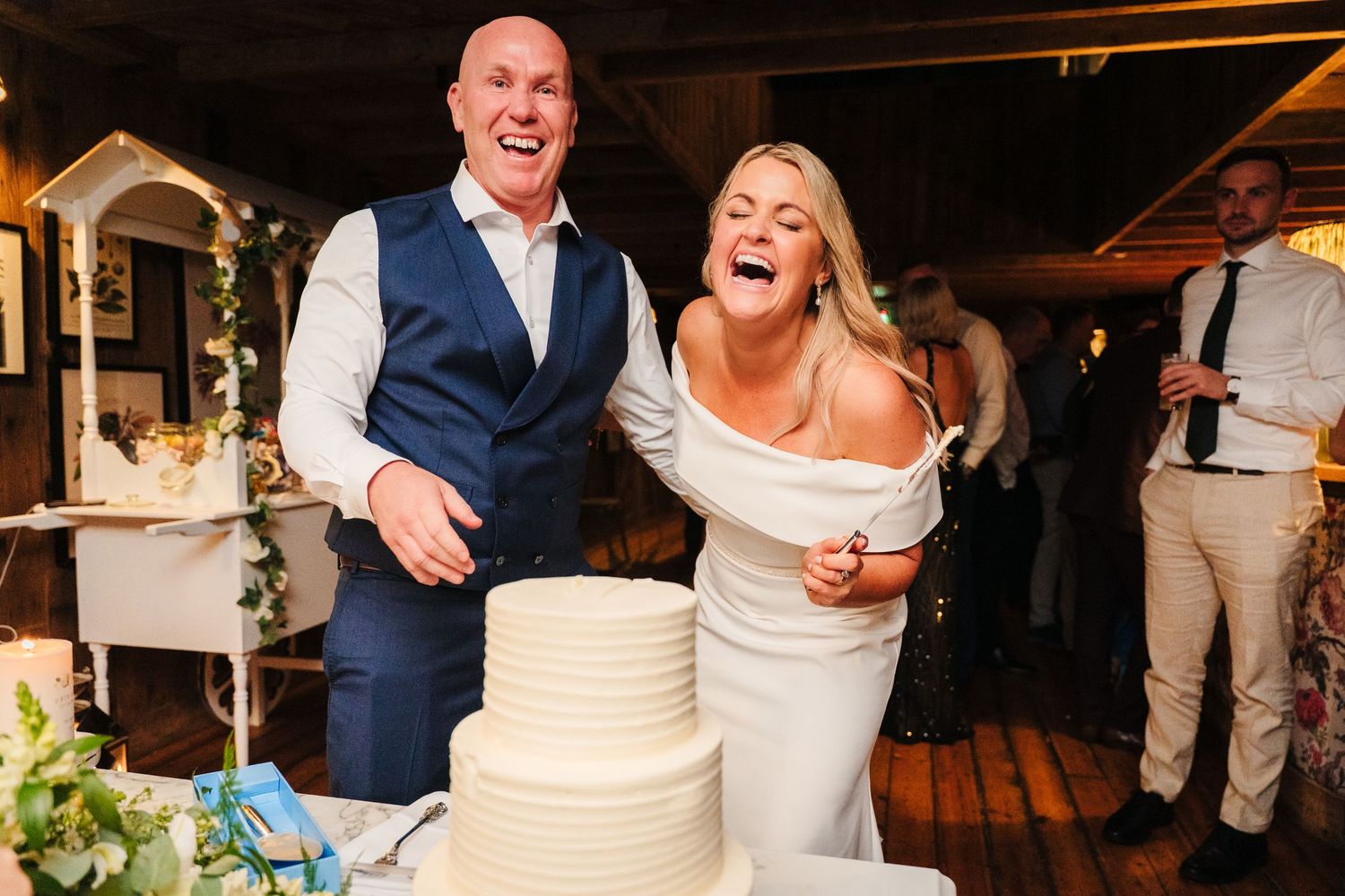 A couple laughs together while cutting their white tiered wedding cake. The Dean Dublin Wedding Photographer