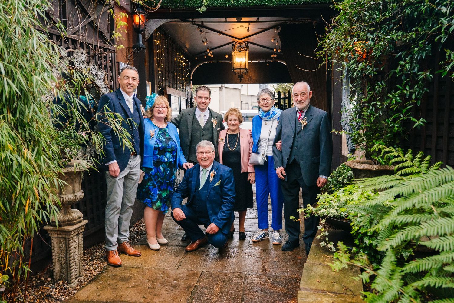Wedding party poses together in lush garden archway.