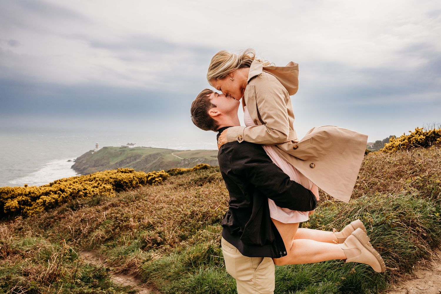 A romantic windswept embrace on a coastal hillside with wildflowers and ocean views in the background. PHOTOGRAPHER Dublin ireland