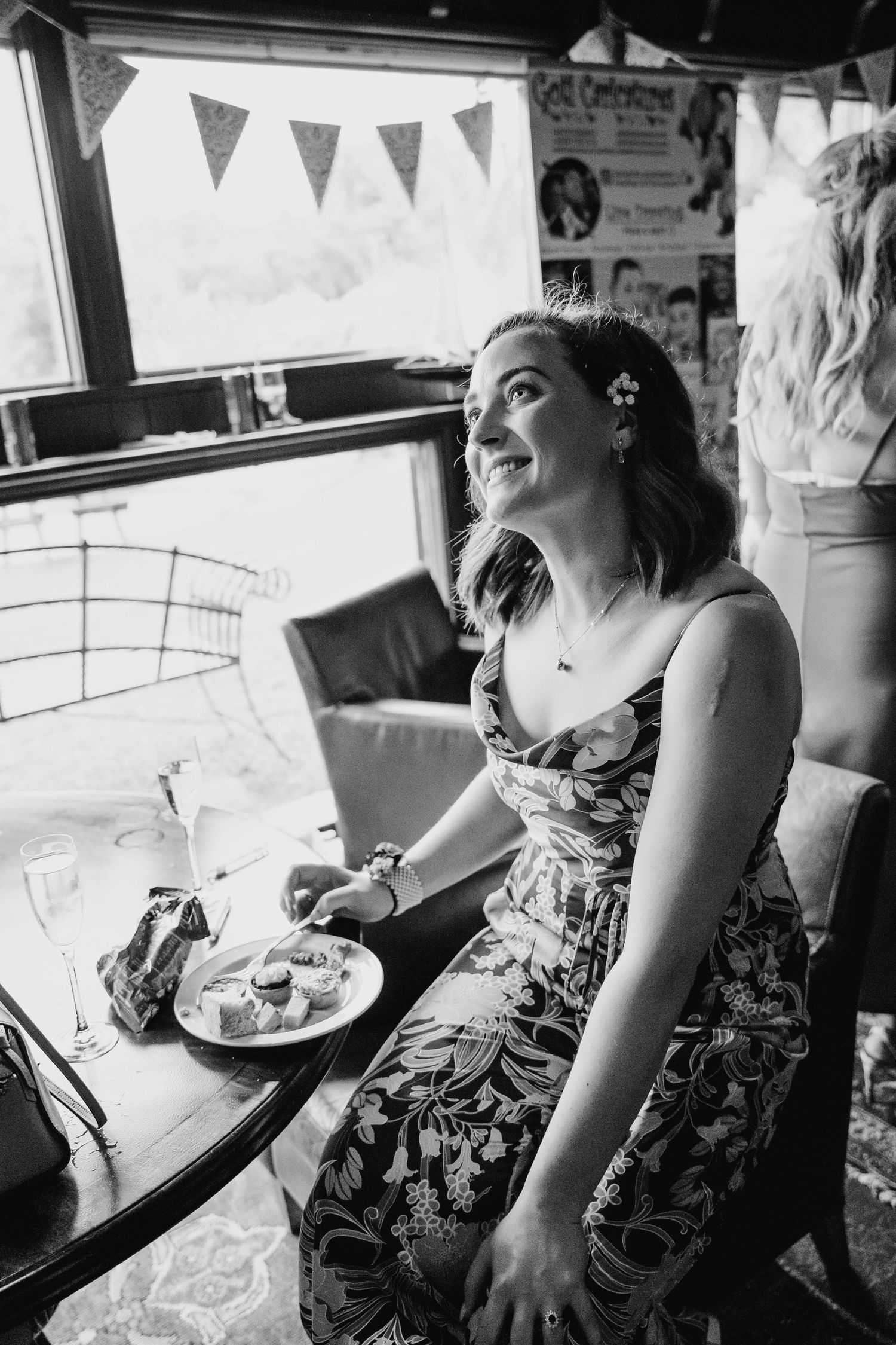 Black and white photo of person in floral dress enjoying refreshments at a party with bunting. Wedding photographer Dublin
