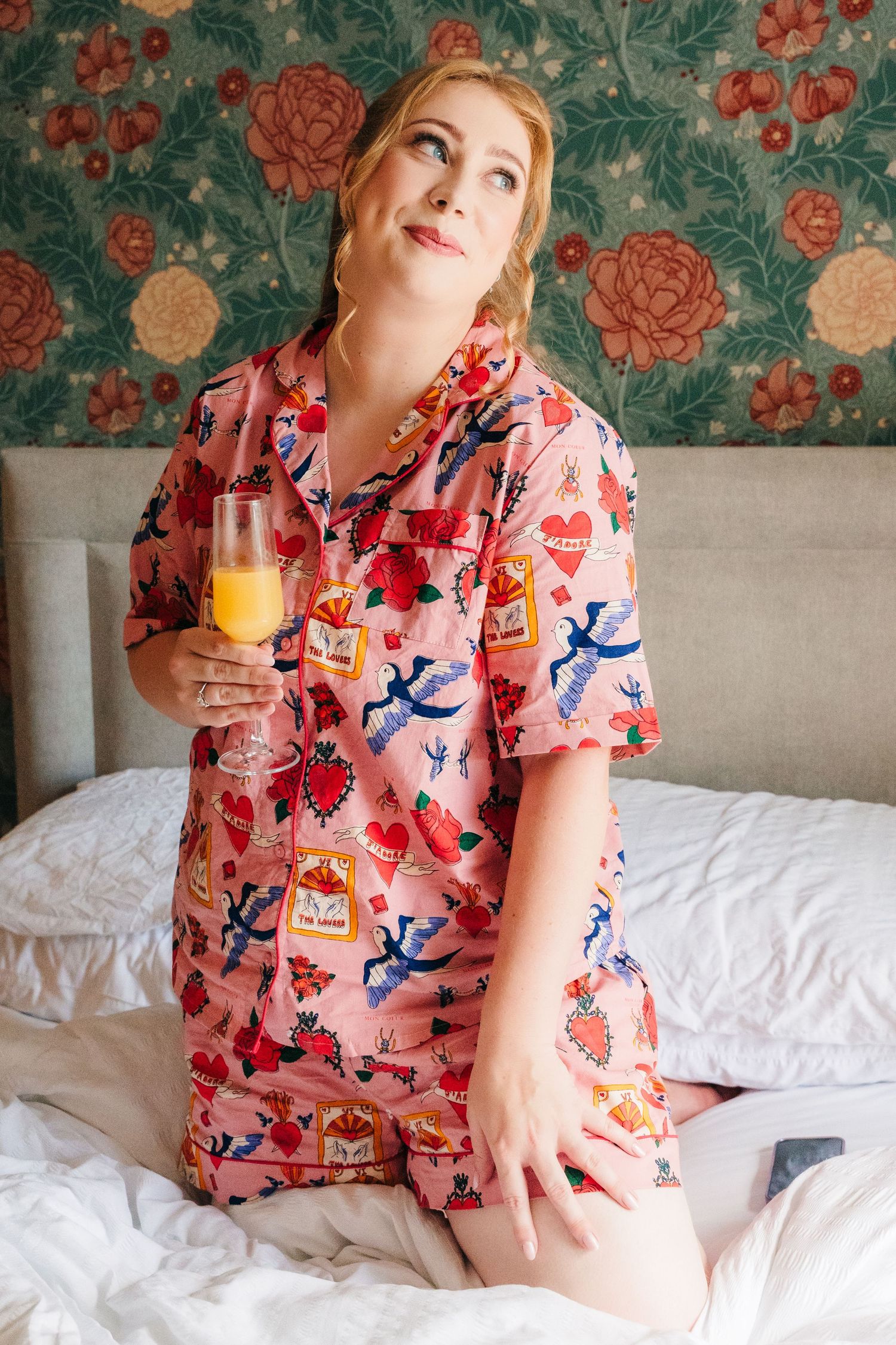 Person relaxing in bed wearing pink floral pajamas while holding orange juice in natural morning light. . Village Barn Tyrrellspass wedding