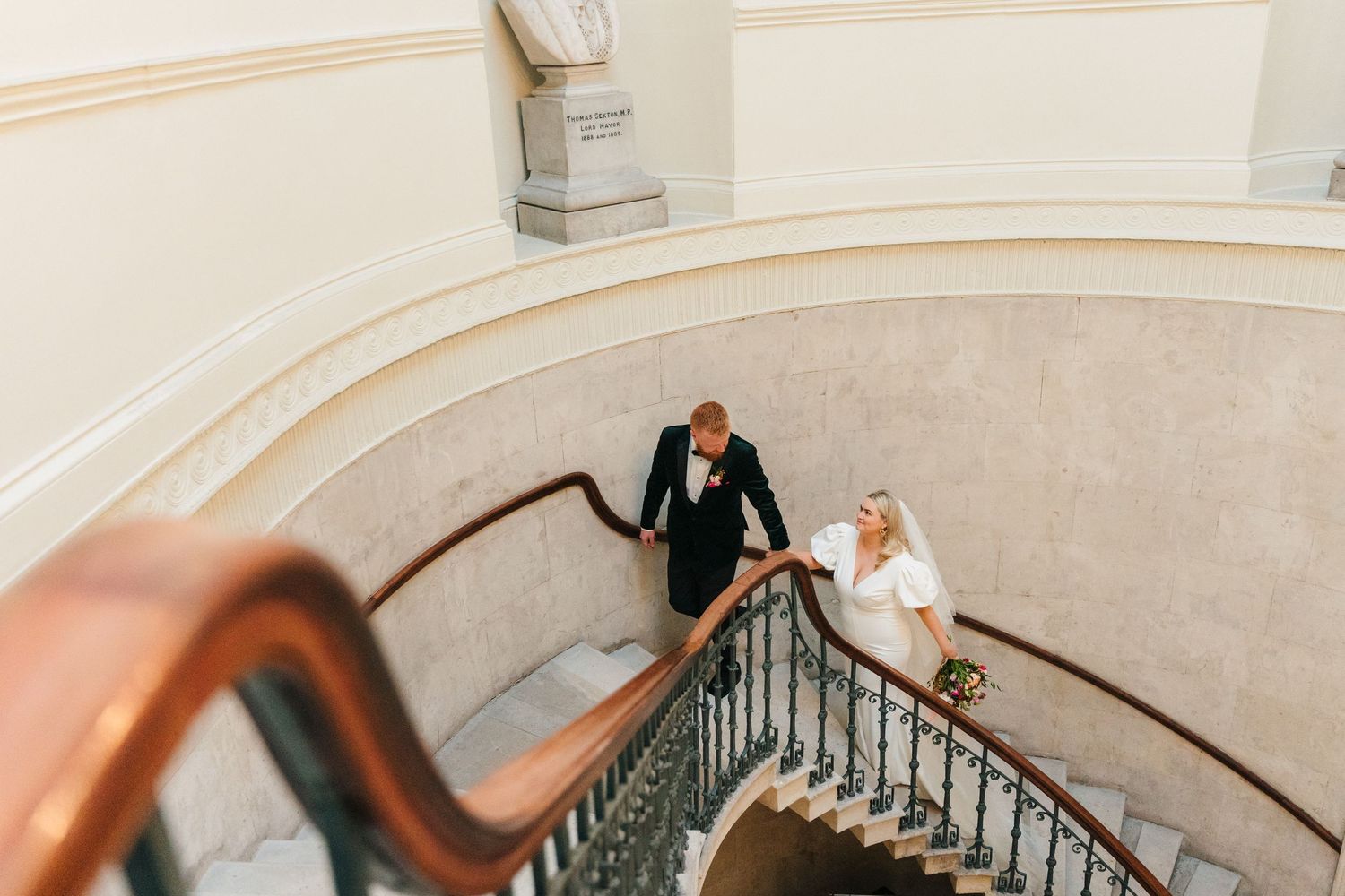 Newlyweds descending an elegant curved staircase with ornate railings captured from above. City Hall Dublin Photographer