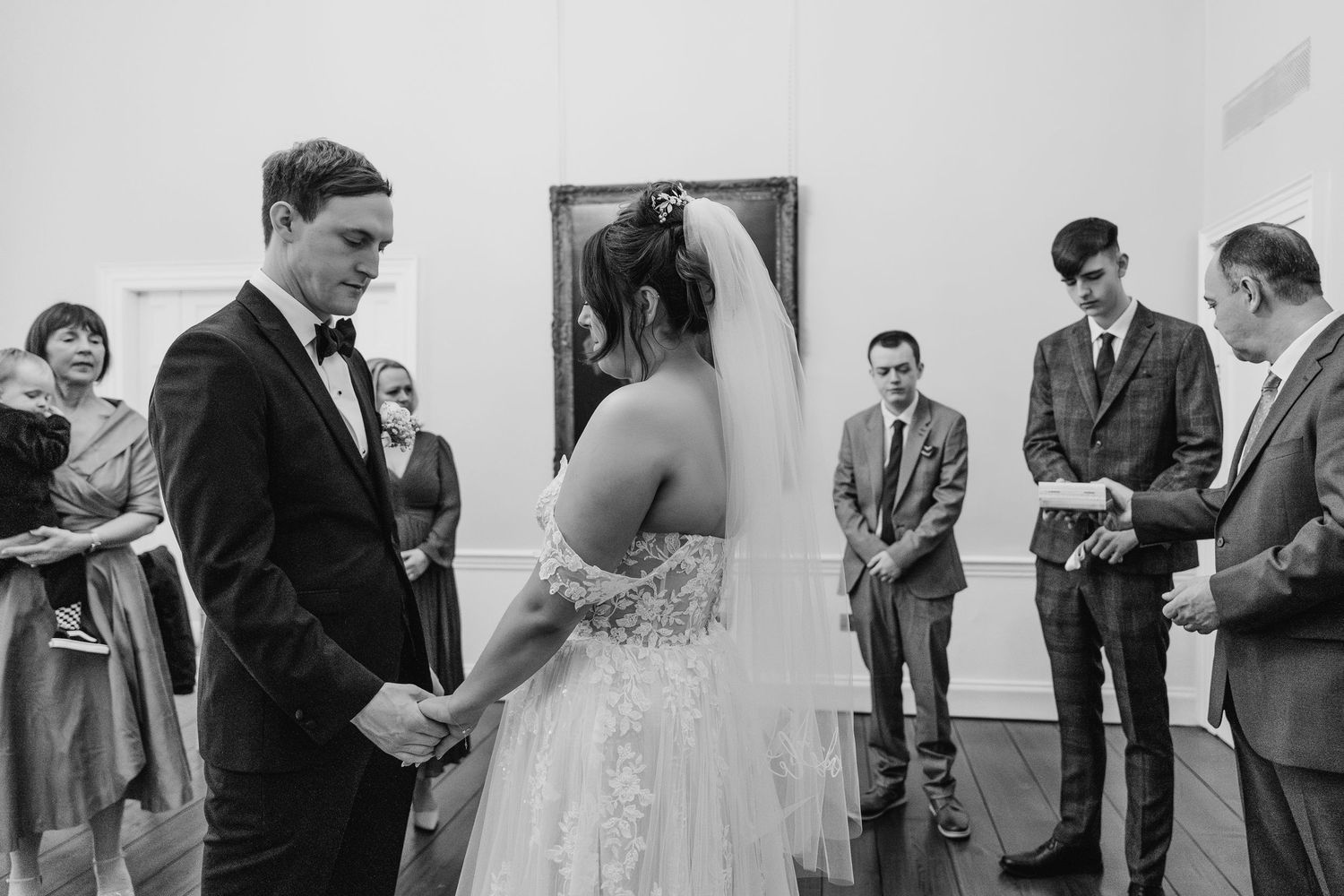 A black and white wedding ceremony photo showing a couple exchanging vows surrounded by wedding attendants.  Wedding PHOTOGRAPHER Dublin