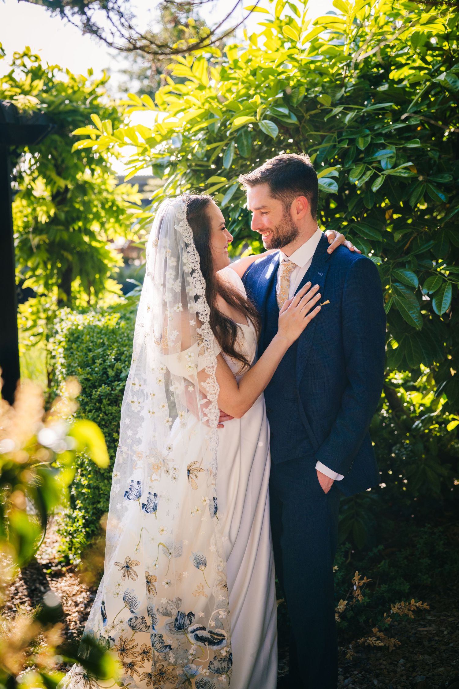 Poulaphouca Wedding photographer wicklow  A romantic wedding couple embraces in a lush garden setting with sunlit foliage.