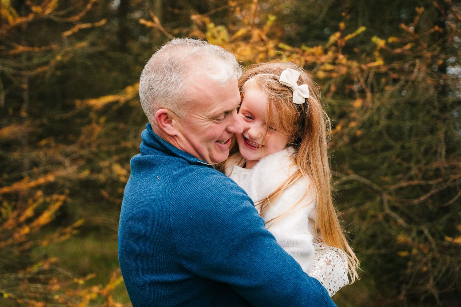 Family Photographer Dublin Ireland Intimate family portrait captured in golden autumn light with trees in background.