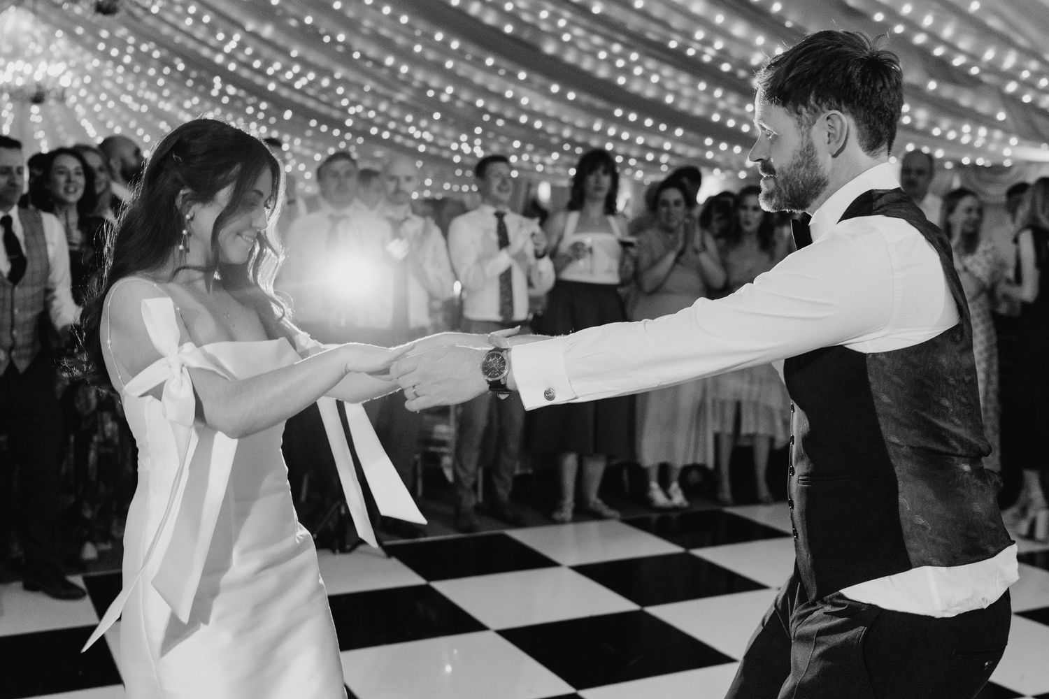 Castle Leslie Wedding PhotoA black and white photo of a couple dancing on a checkered floor under string lights at their wedding reception.