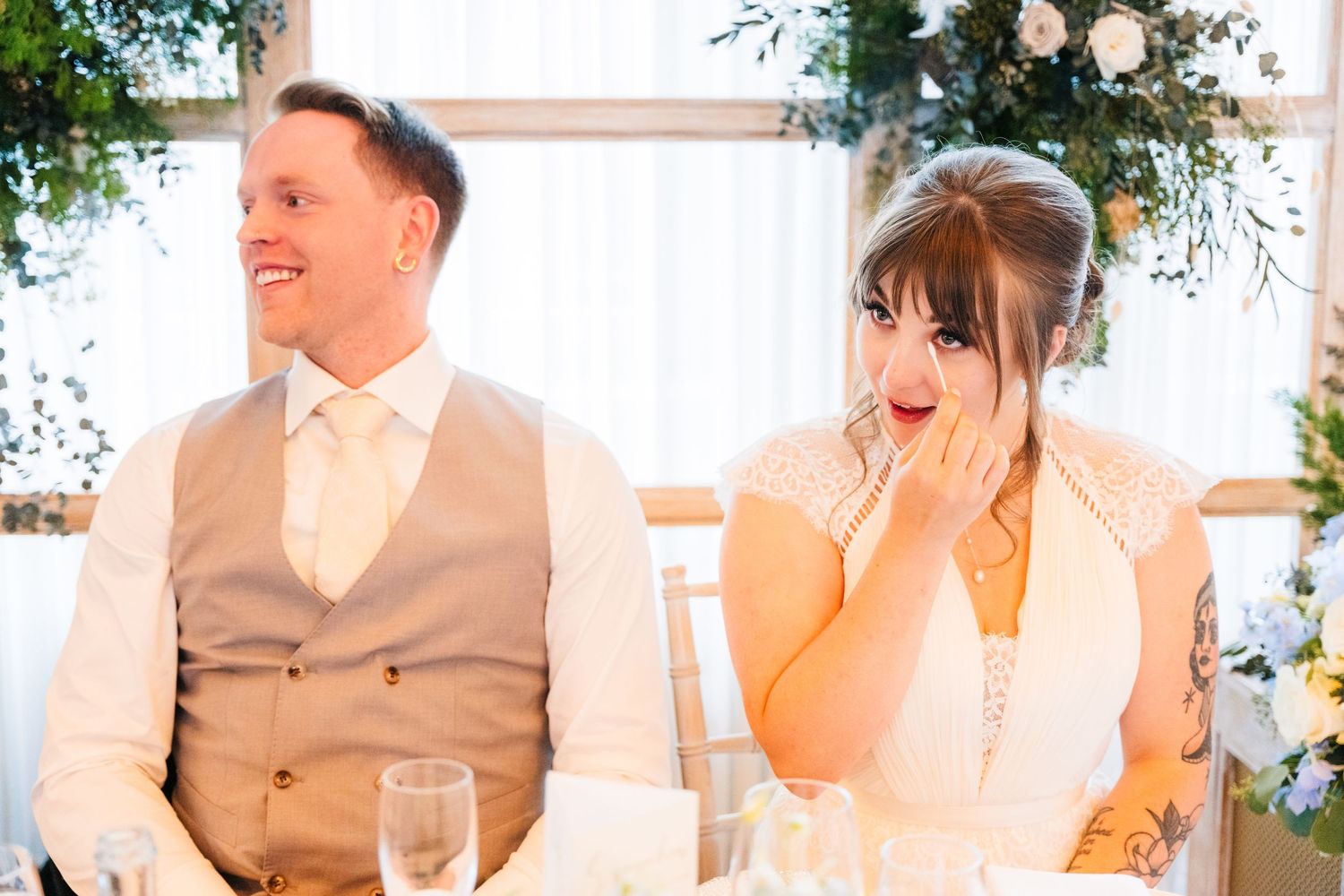 A couple seated at their wedding reception table share an emotional moment surrounded by floral decorations. PHOTOGRAPHER Dublin Ireland Wed