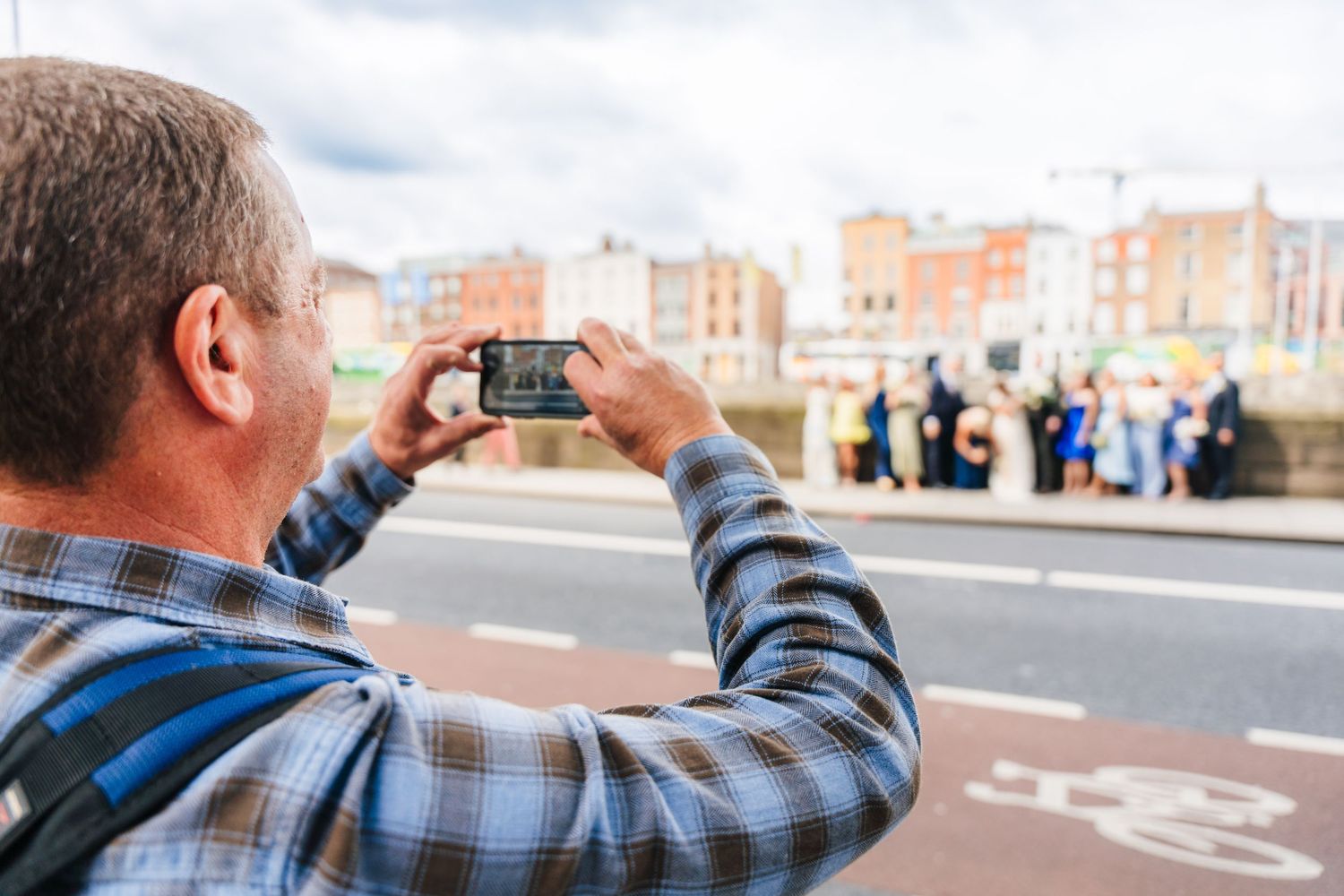 Guest taking photo of wedding party with smartphone on city street. PHOTOGRAPHER Dublin Ireland Wedding