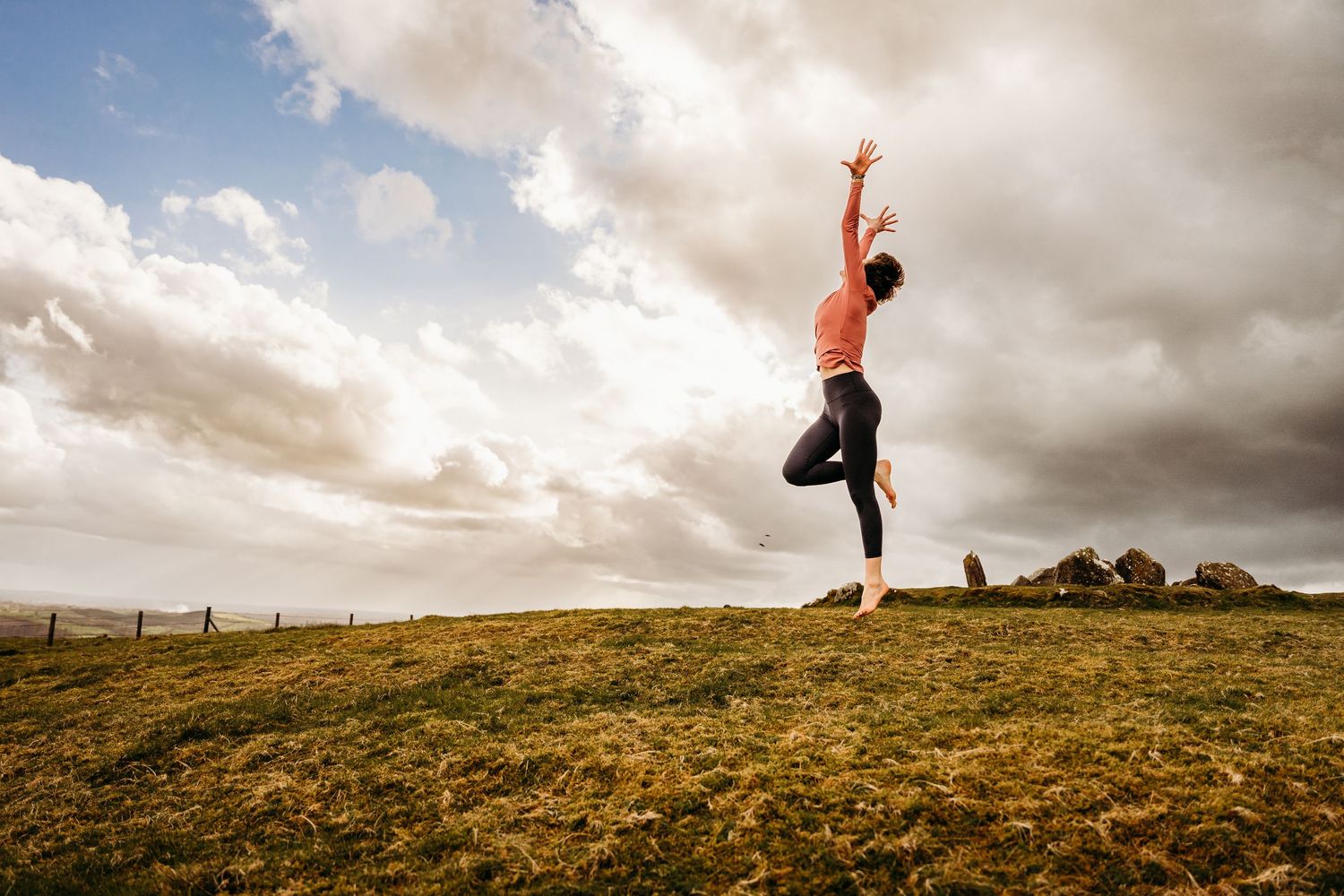 A silhouetted figure strikes graceful poses against a dramatic cloudy sky on a grassy hilltop at sunset. Portrait PHOTOGRAPHER Dublin