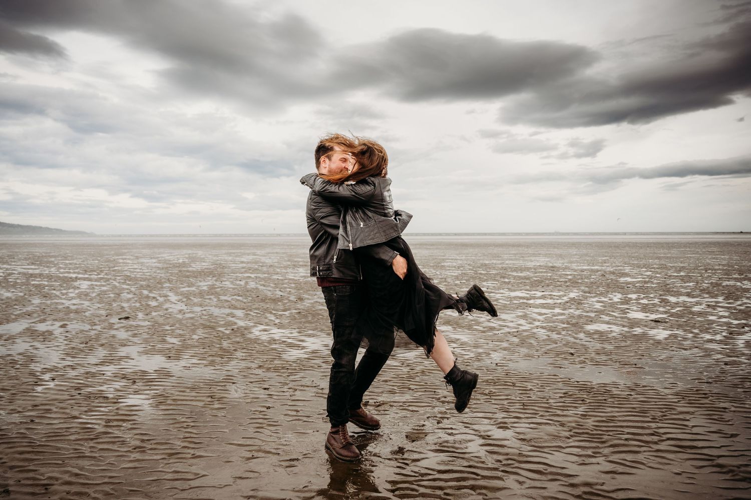 Artistic black and white photos show figures running and dancing along a moody beach under cloudy skies. engagement PHOTOGRAPHER Dublin