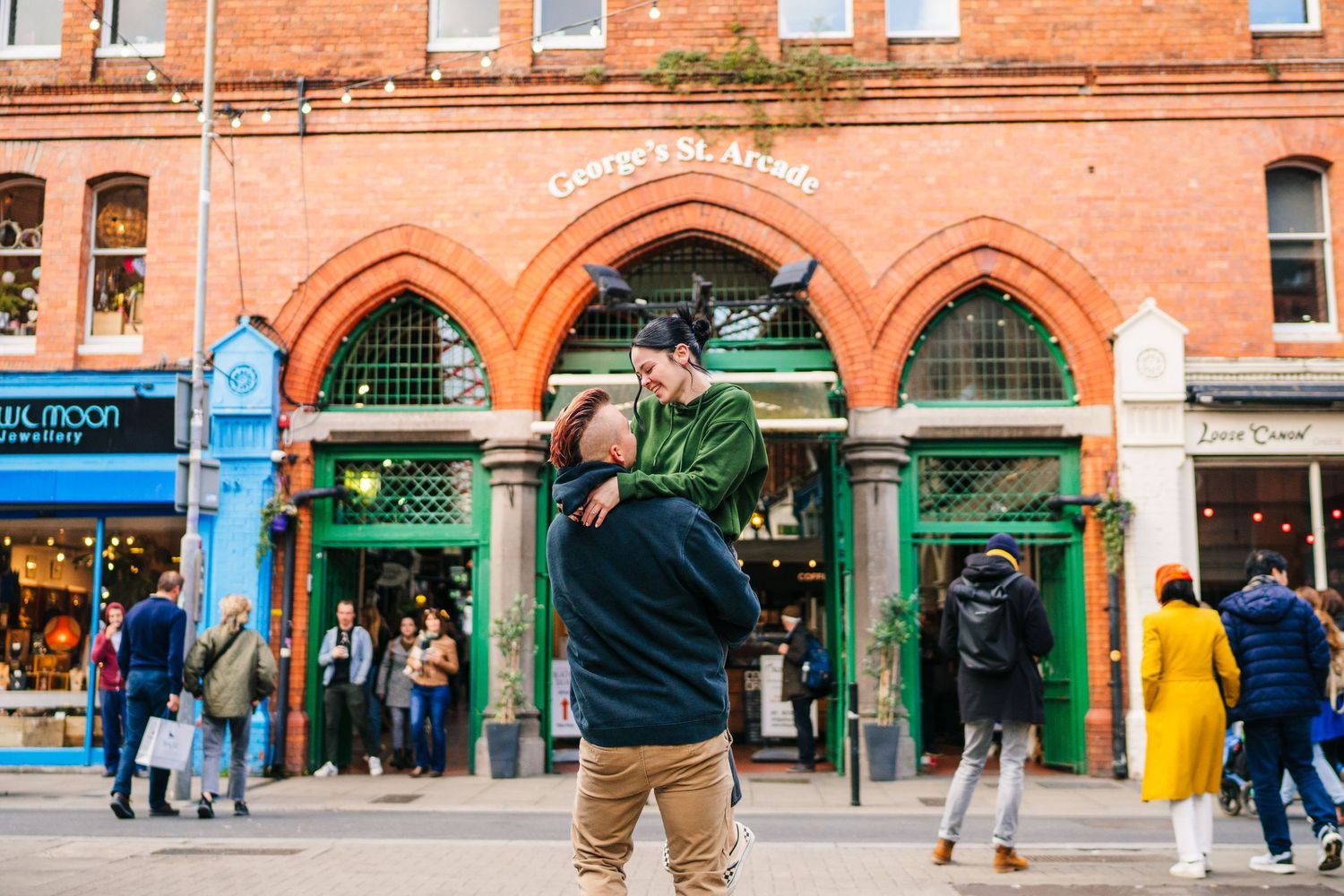 People gather outside a historic brick building with green arched doorways and ornate architectural details. PHOTOGRAPHER Dublin Ireland