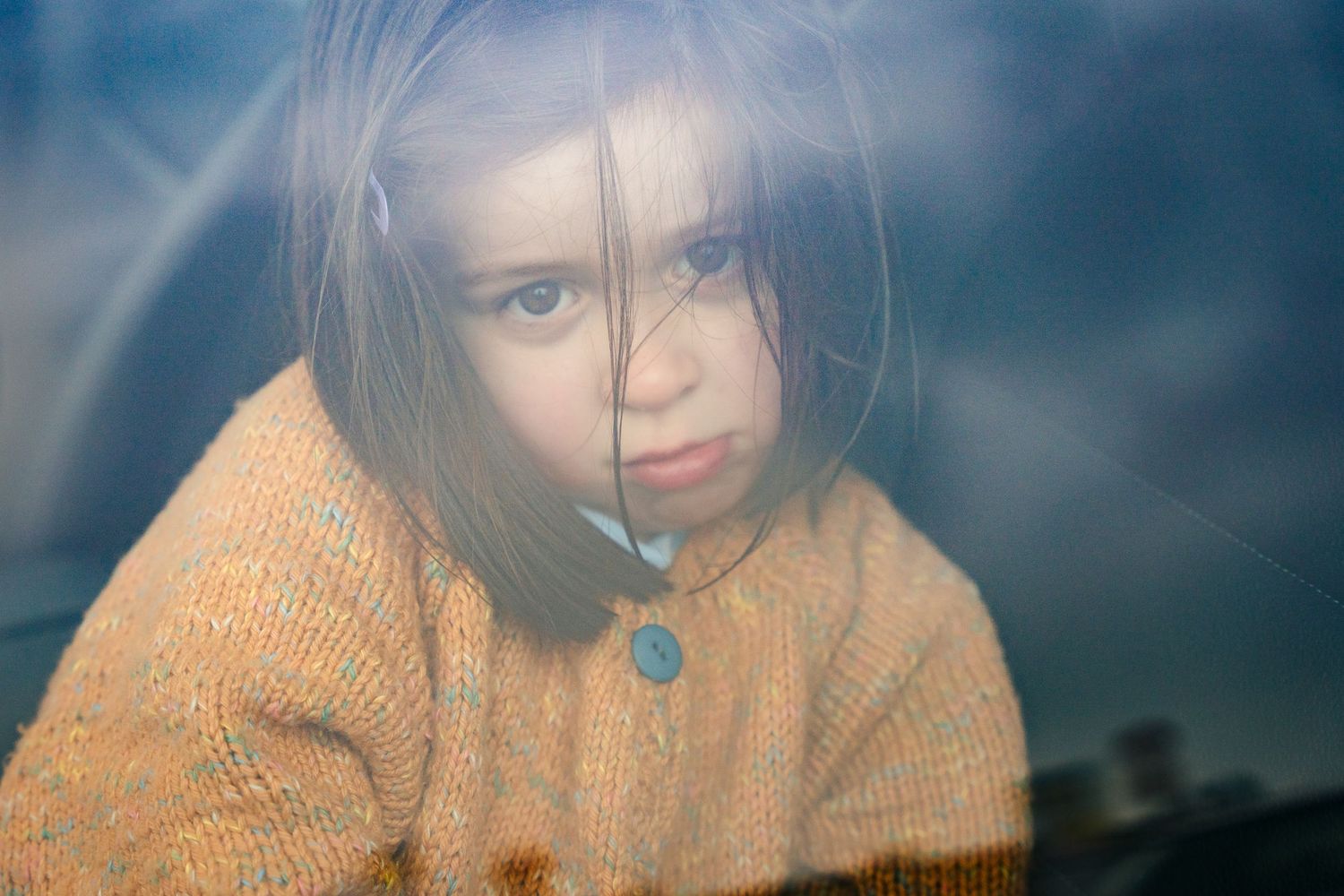 A dreamy portrait through glass with an orange sweater and moody blue background. PHOTOGRAPHER Dublin