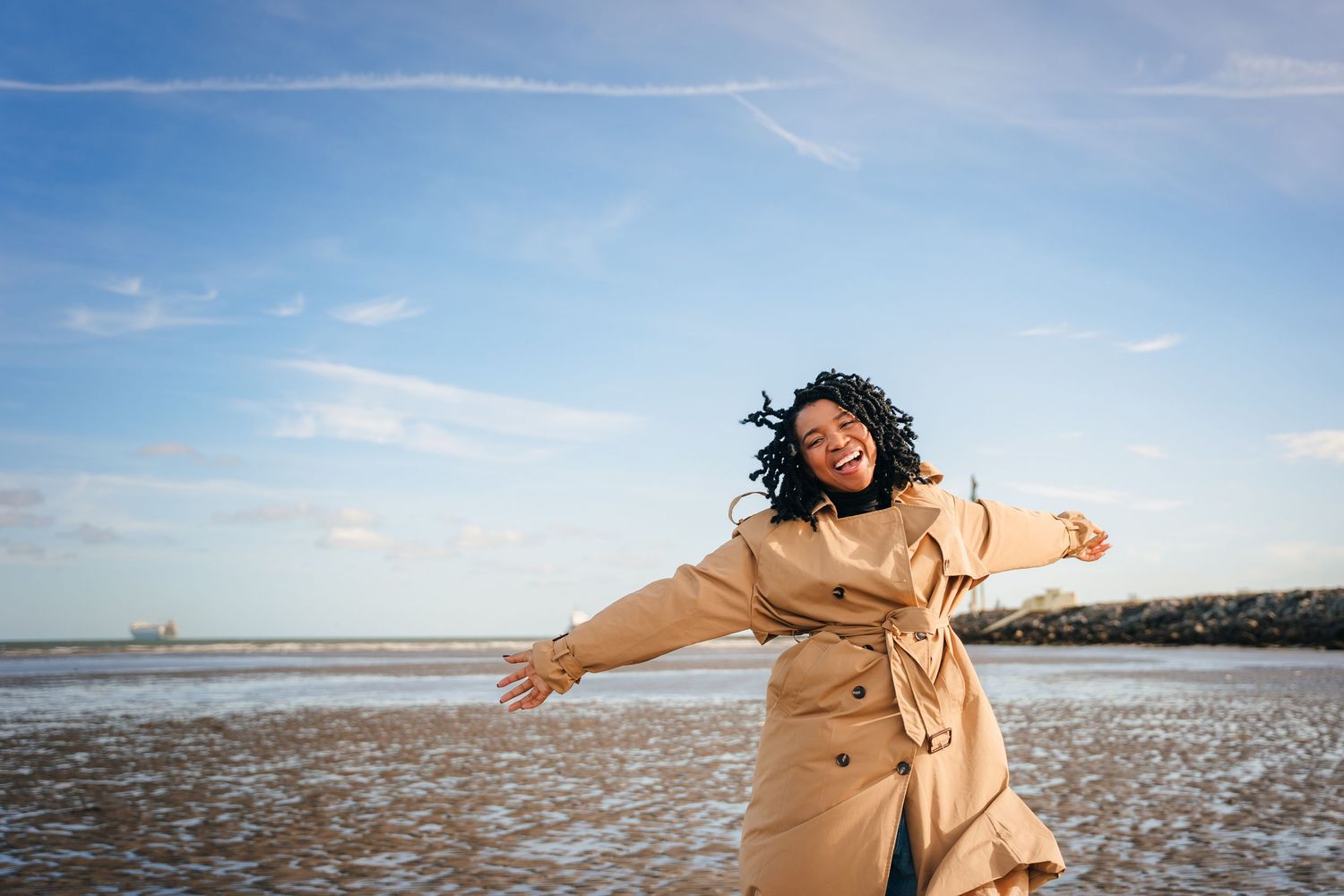 Person in beige trench coat twirling joyfully on beach during sunset with arms outstretched. Dublin professional headshot photographer