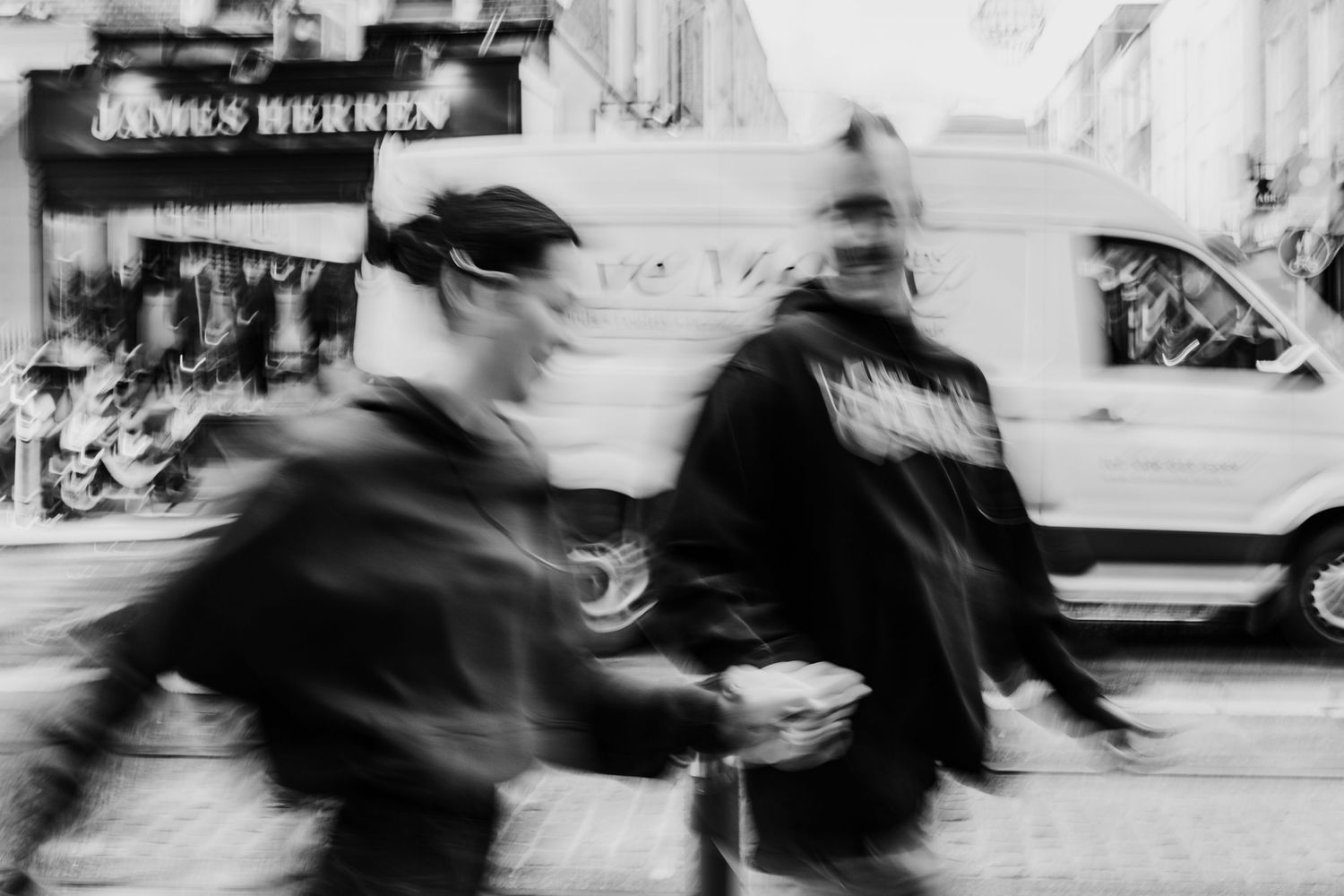 Black and white motion blur photograph of pedestrians walking past storefronts on an urban street. PHOTOGRAPHER Dublin ireland