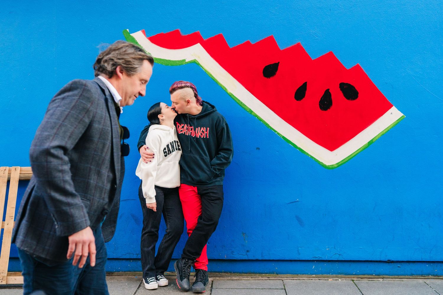 Three people interact in front of a vibrant blue wall with a painted watermelon slice artwork. PHOTOGRAPHER Dublin ireland