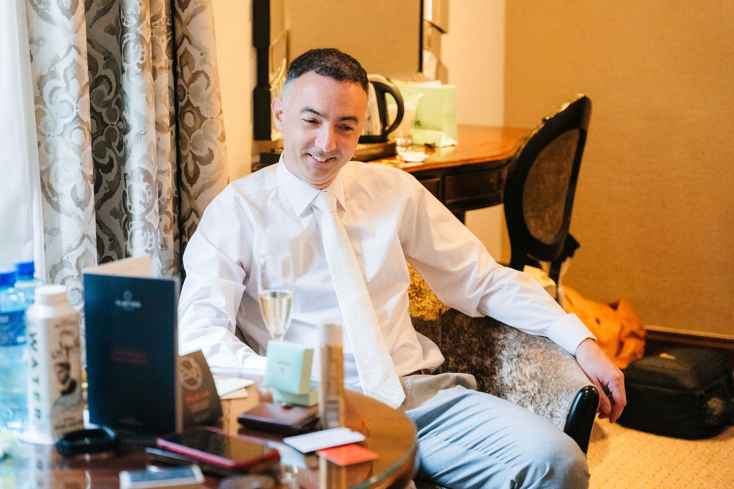 A person in formal attire relaxes in a hotel room chair during wedding preparations. Marco Pierre Dublin Wedding Photographer
