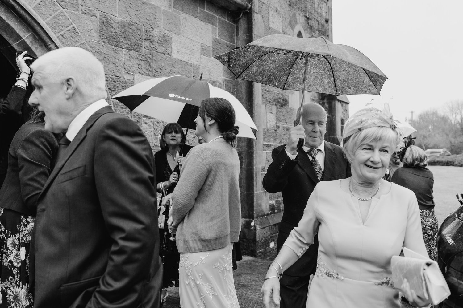 Wedding guests with umbrellas gathering outside church on rainy day.
