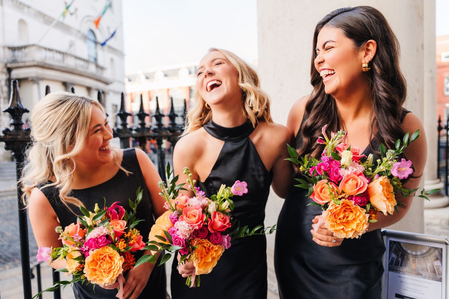 Bridesmaids in black dresses carry vibrant orange and pink bouquets while posing along a stone balustrade. Wedding photographer dublin