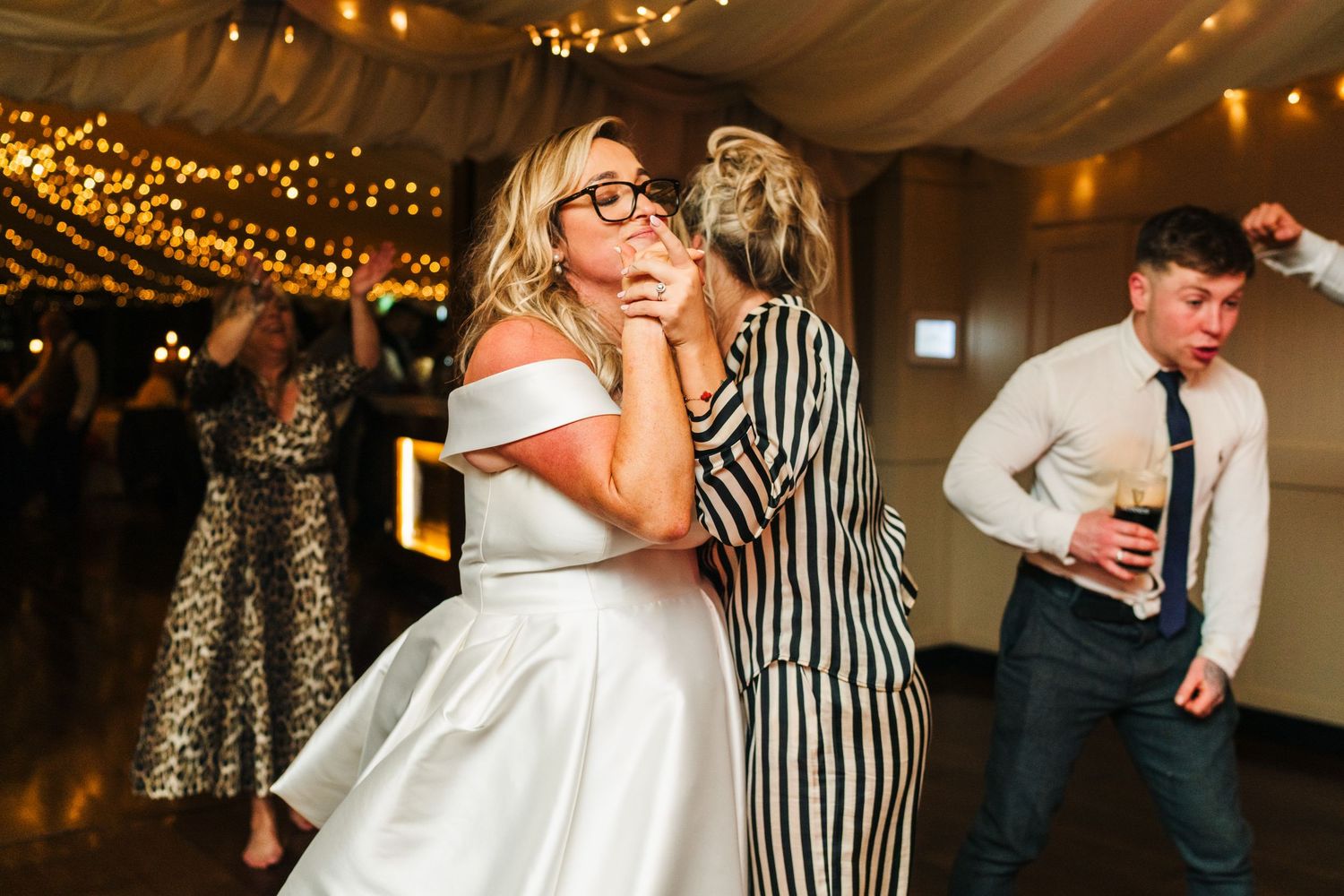 A wedding reception scene with guests dancing under warm string lights.  Virginia Park Lodge Wedding Photographer Cavan Dublin Ireland