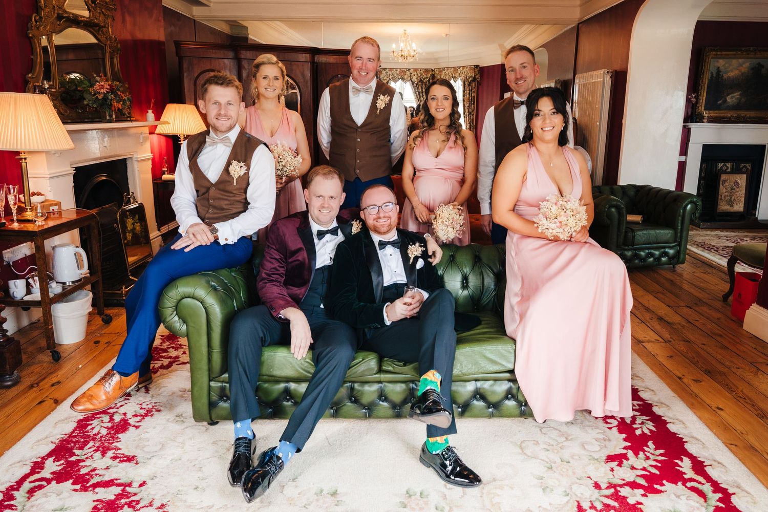 A group poses together on a green velvet couch in formal attire during a wedding celebration. LGBTQ Ashley Park Wedding Photographer