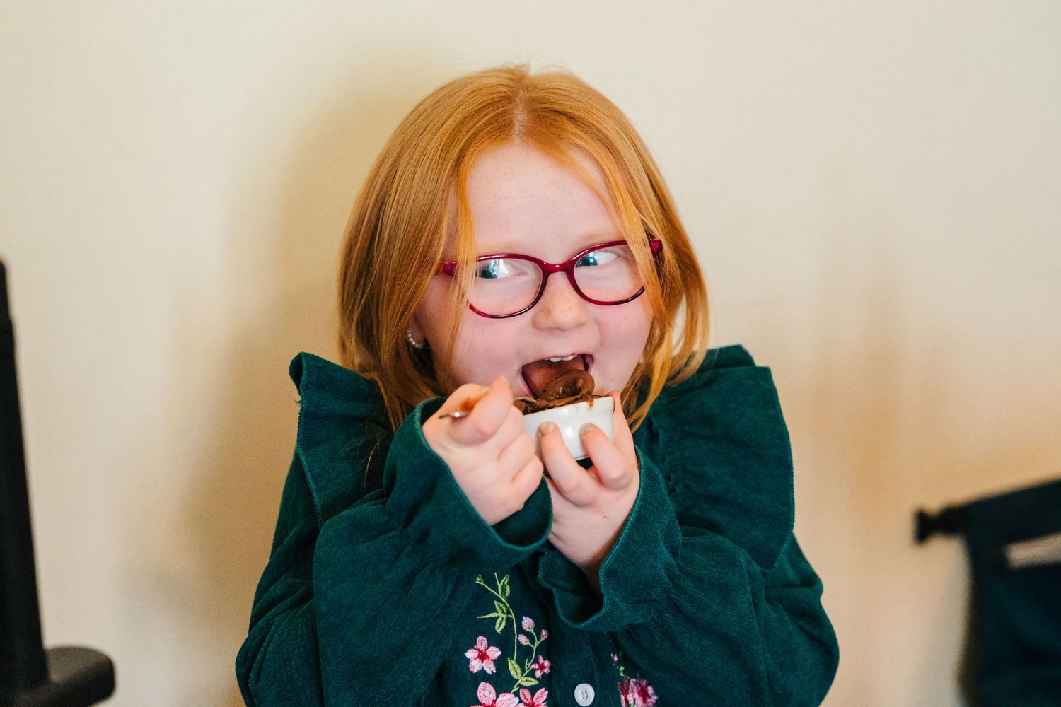 A child wearing glasses and a dark green sweater takes a big bite of something while looking straight at the camera.  Wedding PHOTOGRAPHER T