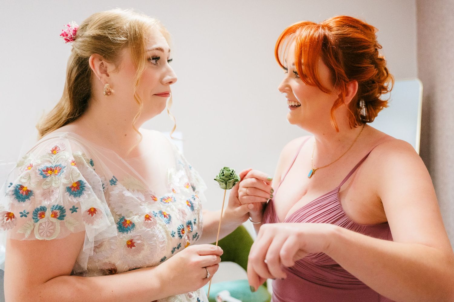 Two women sharing a heartfelt moment at a wedding, one wearing a floral dress and one in pink. . Village Barn Tyrrellspass wedding photograp