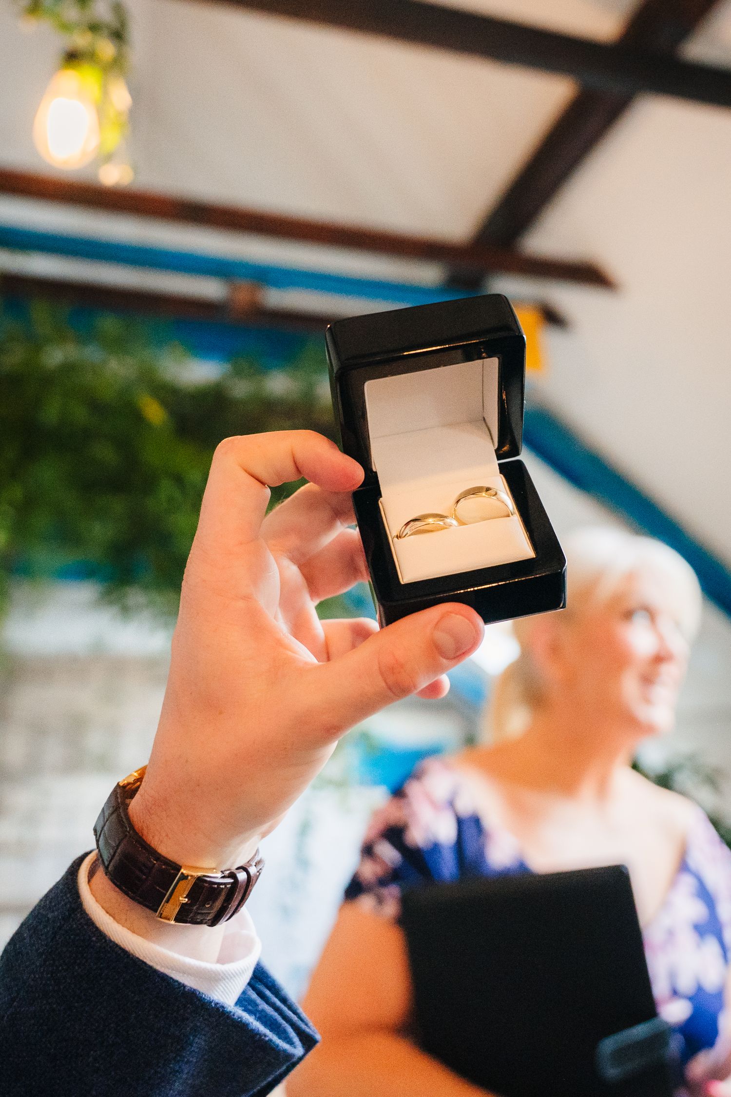 Wedding rings displayed in a black box with someone blurred in background. Same sex wedding PHOTOGRAPHER Dublin