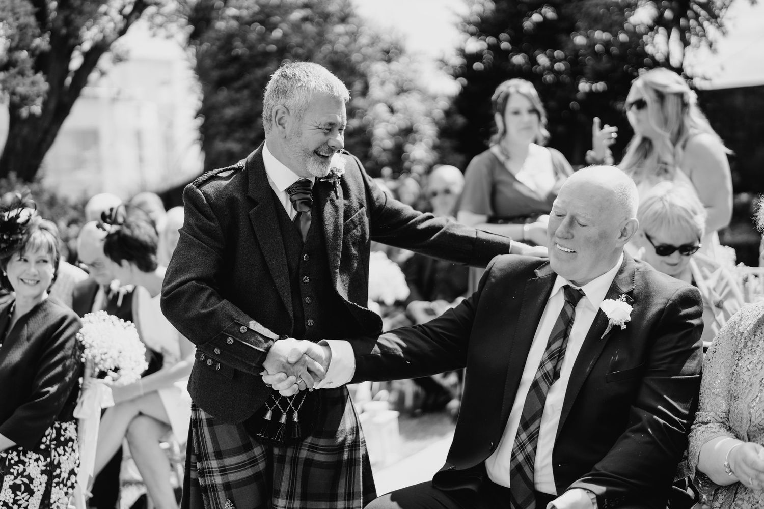 Guests celebrating at an outdoor wedding reception with trees and sunlight in the background. Portmarnock Hotel Wedding PHOTOGRAPHER Dublin