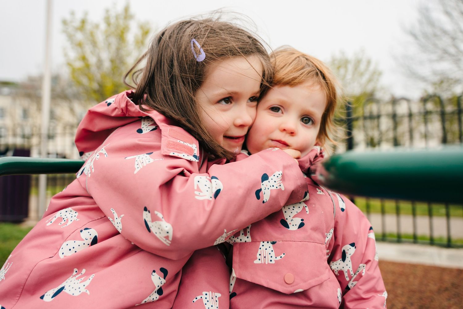 Two figures in matching pink coats share a joyful embrace while playing outdoors in a park setting. PHOTOGRAPHER Dublin