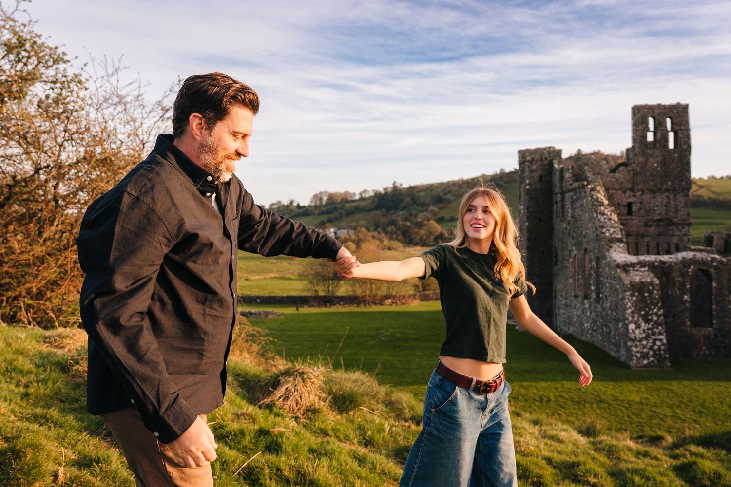 Playful outdoor engagement session at historic stone castle ruins surrounded by green fields. Photographer Ireland dublin