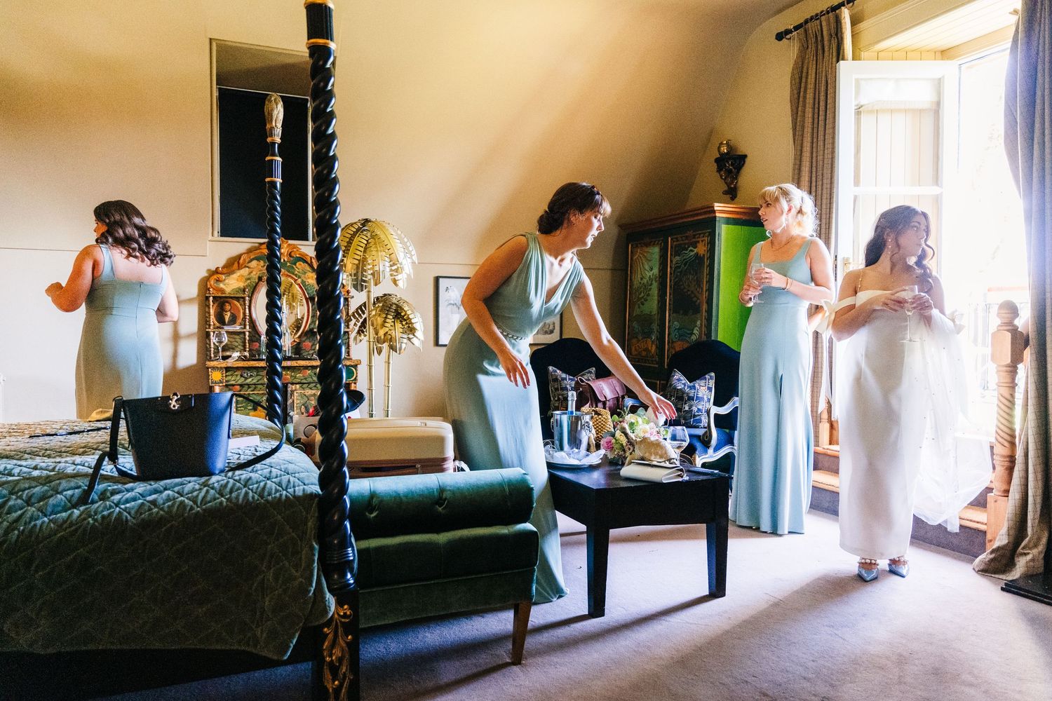 Several figures in blue dresses gather in an elegant bedroom while preparing for a formal event. Castle Leslie Wedding Photographer Dublin