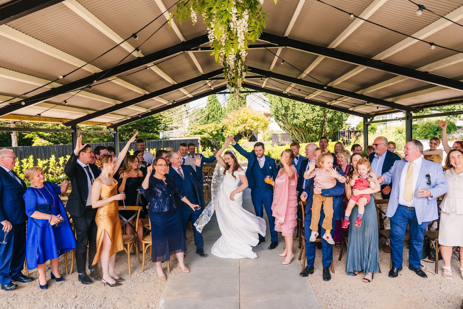 Poulaphouca Wedding photographer wicklow  Large group of wedding guests celebrating under covered outdoor venue with hanging greenery.