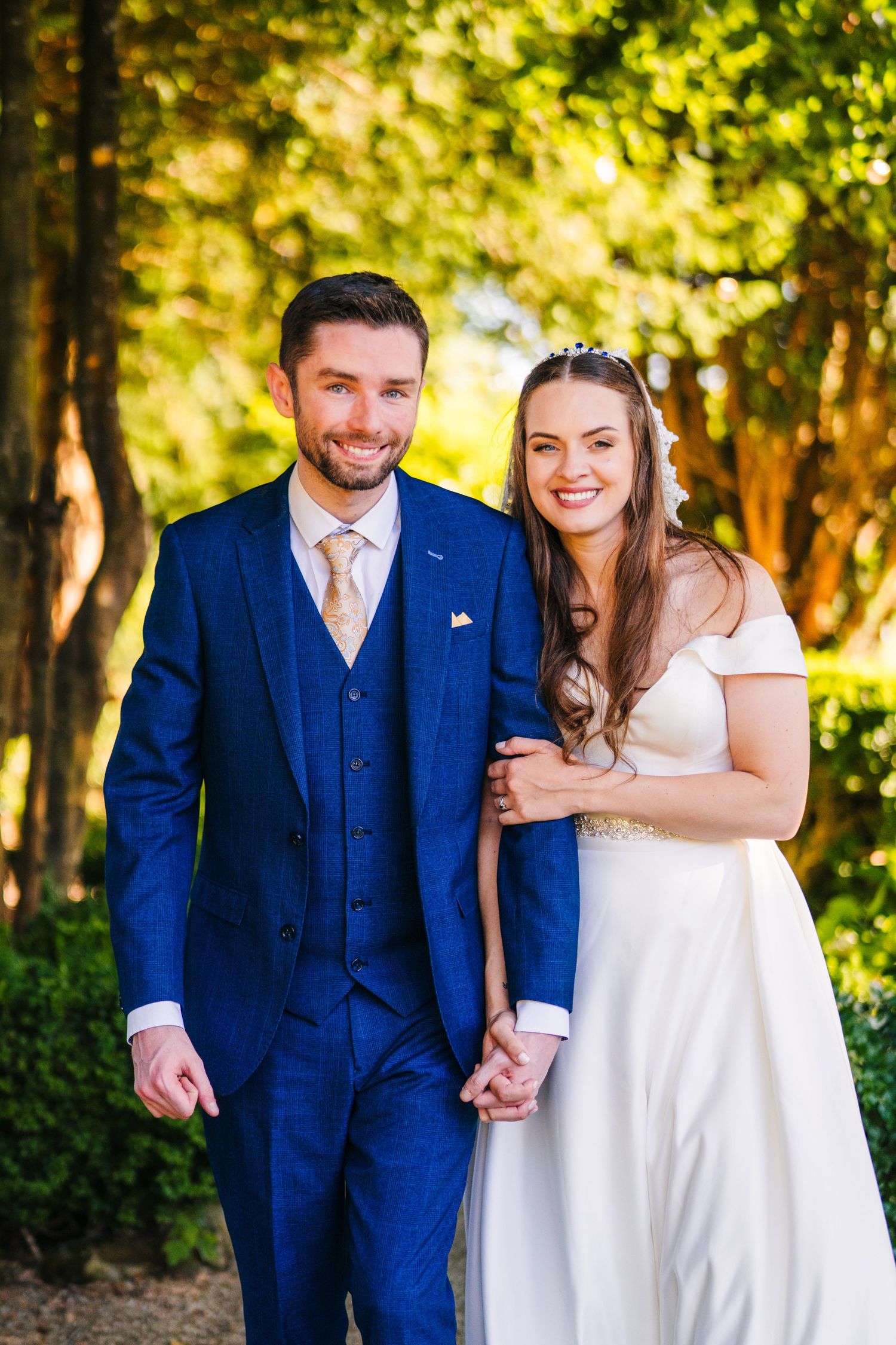 Poulaphouca Wedding photographer wicklA wedding couple poses together on a wooded path with beautiful golden sunlit trees in the background.
