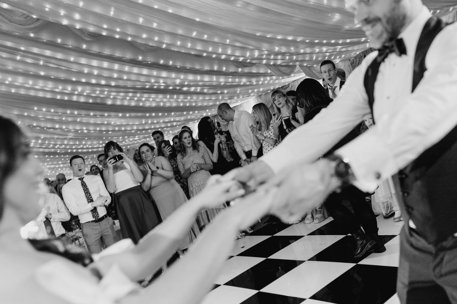Castle Leslie Wedding Photographer Dublin Black and white photo of wedding guests dancing in a line on a checkered dance floor.