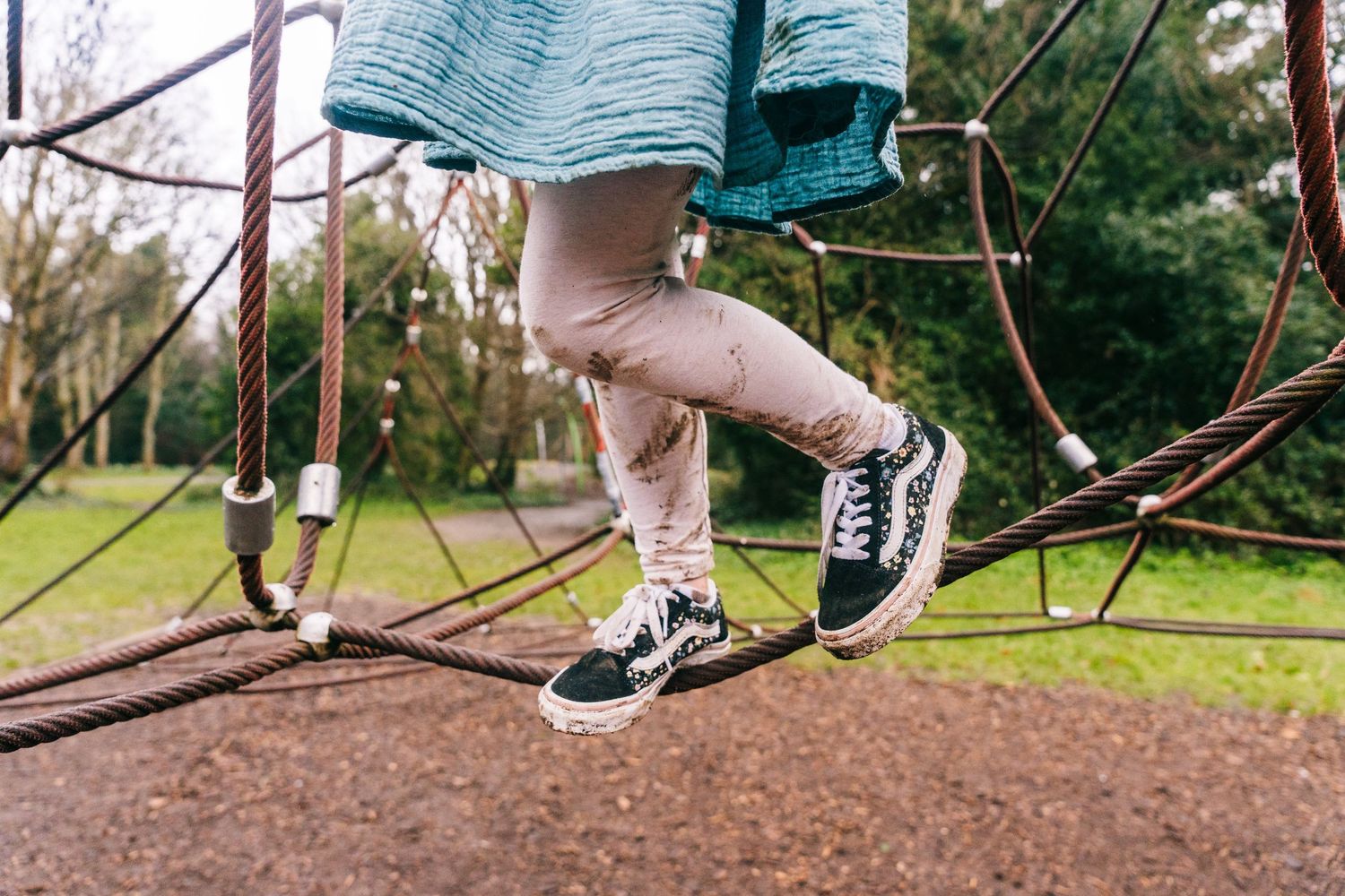 Family photographer Dublin Ireland  Close-up of sneakers and legs on playground equipment against mulch ground.