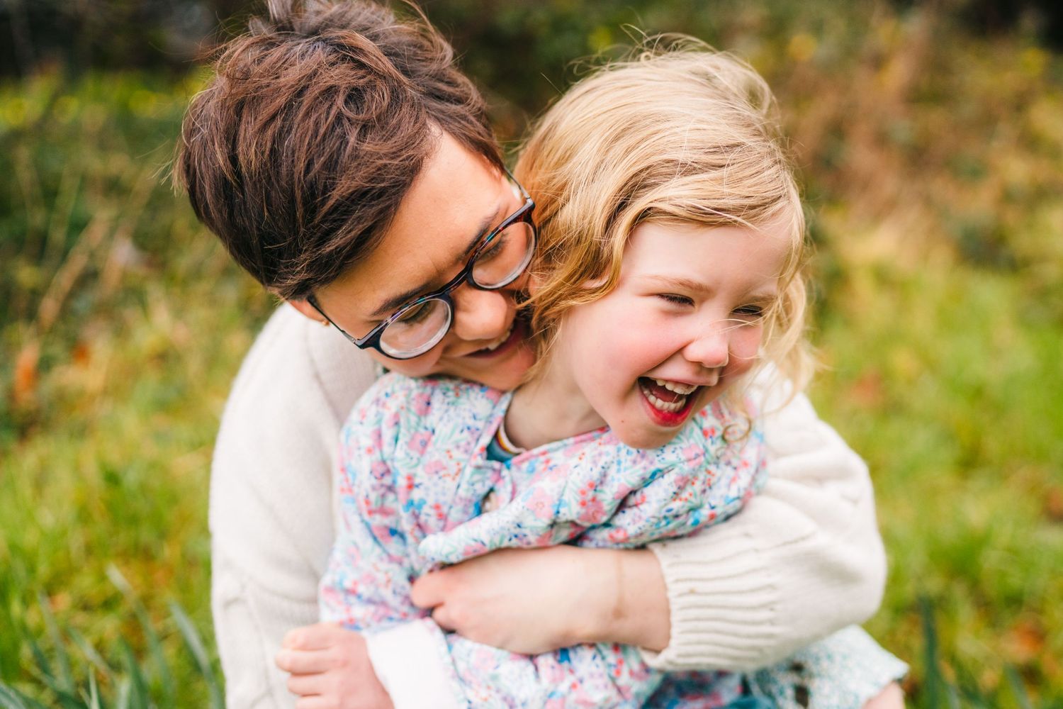 A joyful moment captured outdoors with a warm embrace and laughter against a natural green background. Family photographer Dublin Ireland