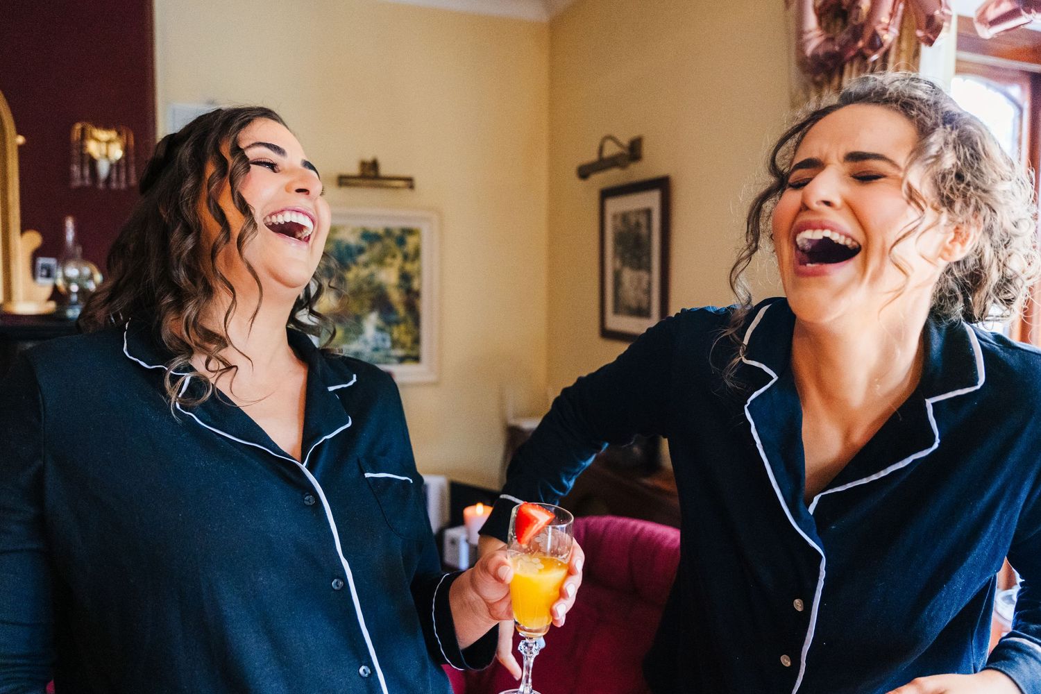 Two people wearing matching navy blue pajamas share a joyful laugh while one holds a colorful cocktail. Millhouse slane wedding photographer