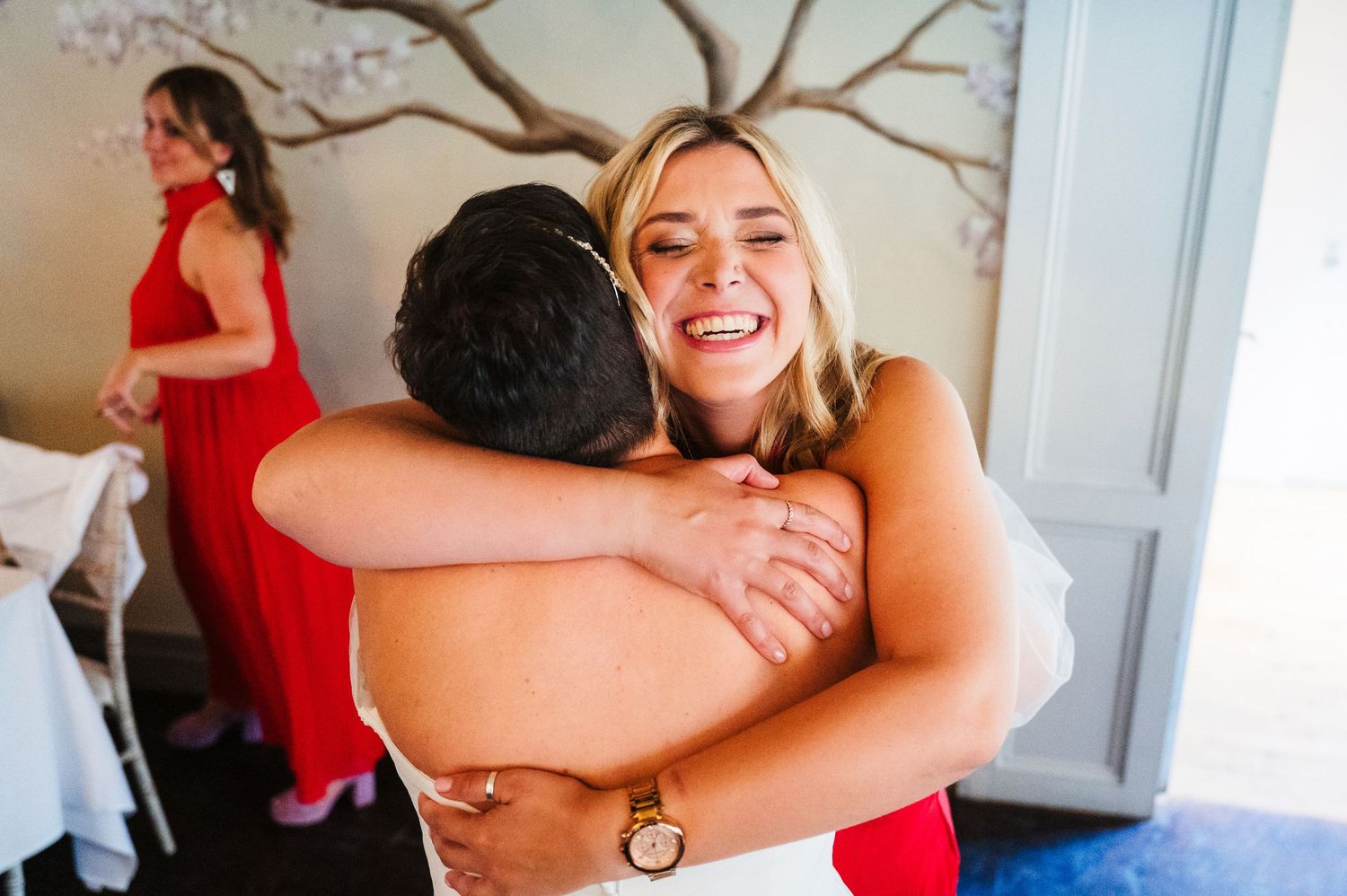 Millhouse slane wedding photographer dublin Wedding guests share joyful hugs during celebration while wearing red dresses.