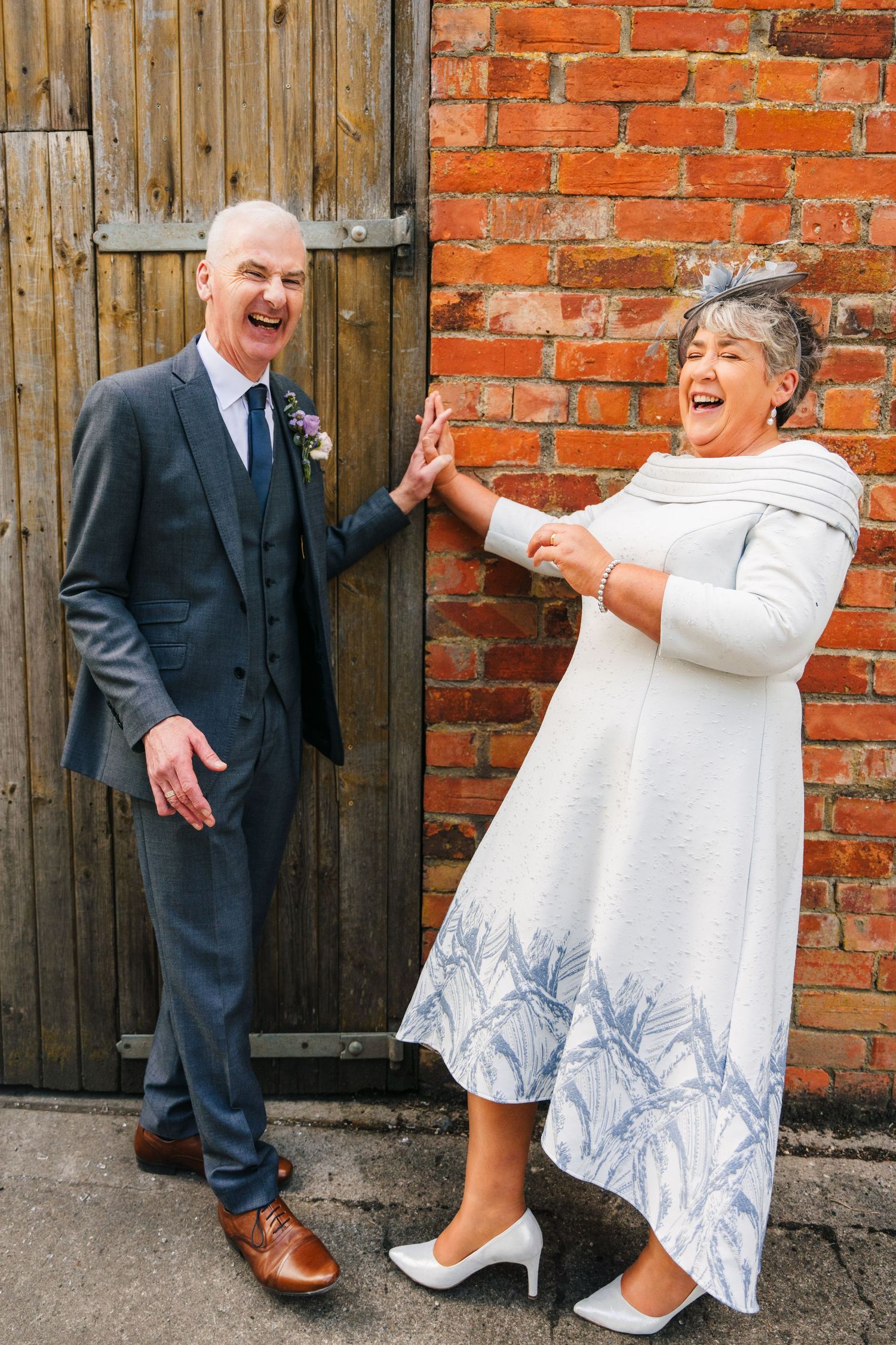 Millhouse slane wedding photographer dublin A couple shares a joyful candid moment against a brick wall backdrop at a formal event.