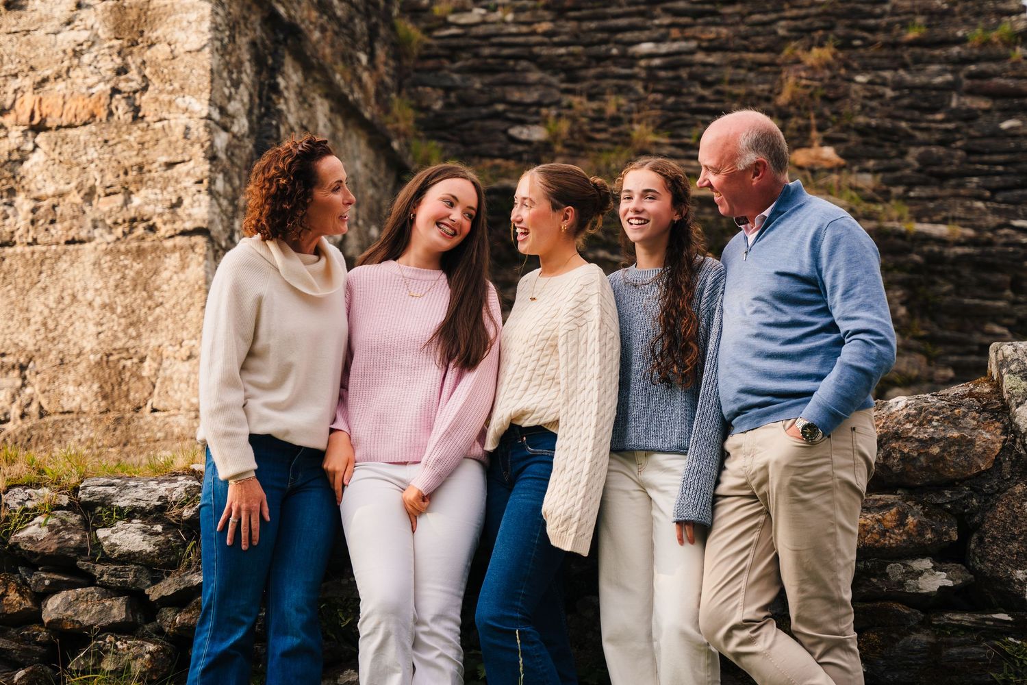 Family photographer Ireland Dublin Several people gathered by a weathered stone wall during an outdoor photoshoot.
