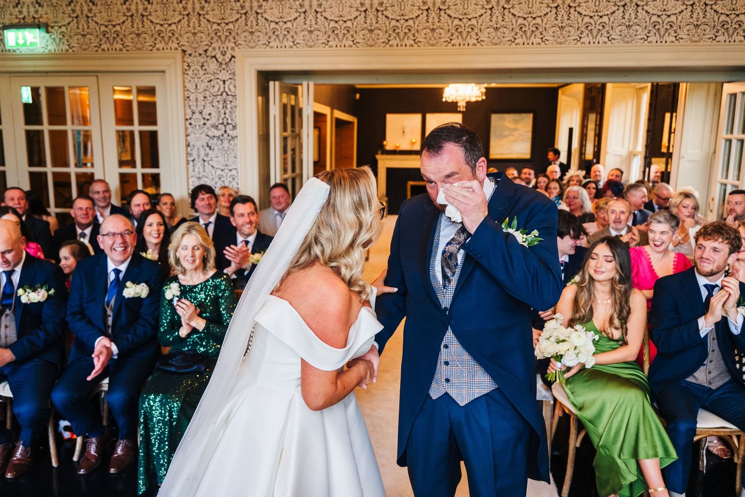 Wedding guests fill an ornate reception hall with decorative wallpaper and chandeliers.  Virginia Park Lodge Wedding Photographer Cavan Dubl