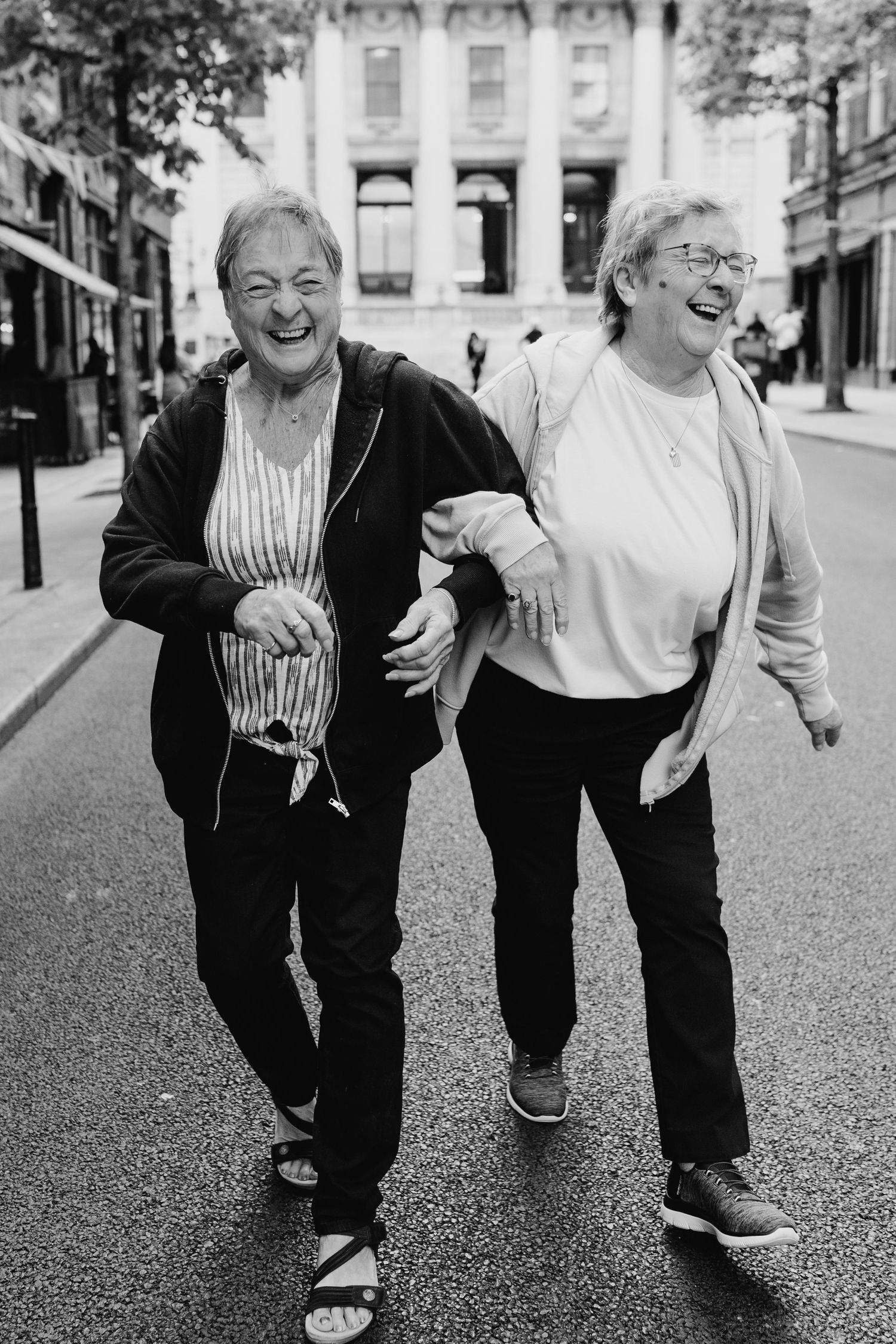 A black and white photo shows people bent over with laughter while walking on a city street. Family photographer Dublin Ireland