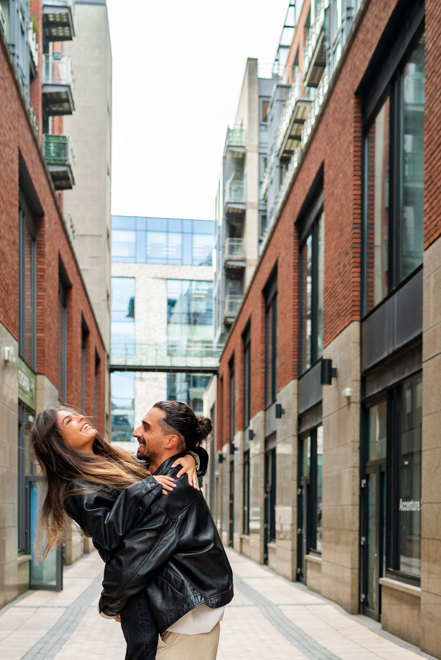 A couple shares playful and romantic moments in an urban setting with brick buildings. Couple's Photoshoot PHOTOGRAPHER Dublin